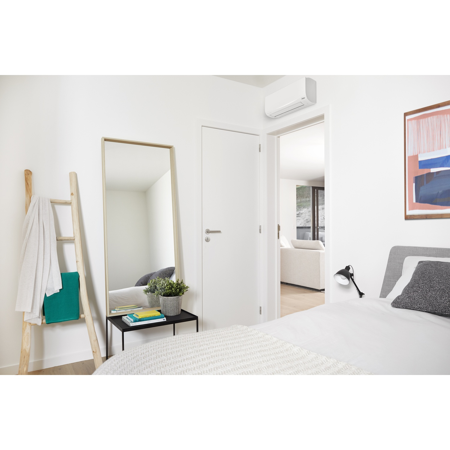 Camera da letto con specchio, condizionatore, scala con asciugamano, letto e quadro.