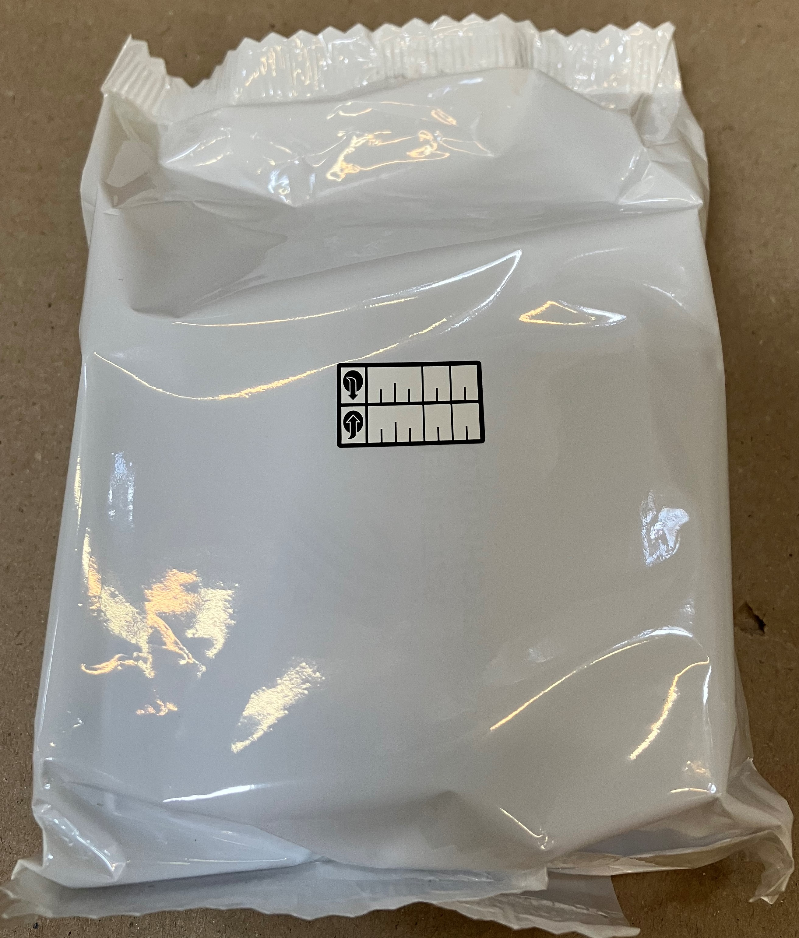 Biały, zapieczętowany pakiet z czarnymi oznaczeniami. Tło to jasnobrązowa powierzchnia.