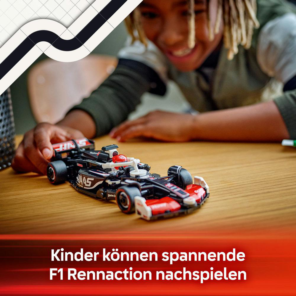 Ein lächelnder Junge spielt mit einem roten und schwarzen Spielzeug-F1-Rennwagen auf einem Holztisch.