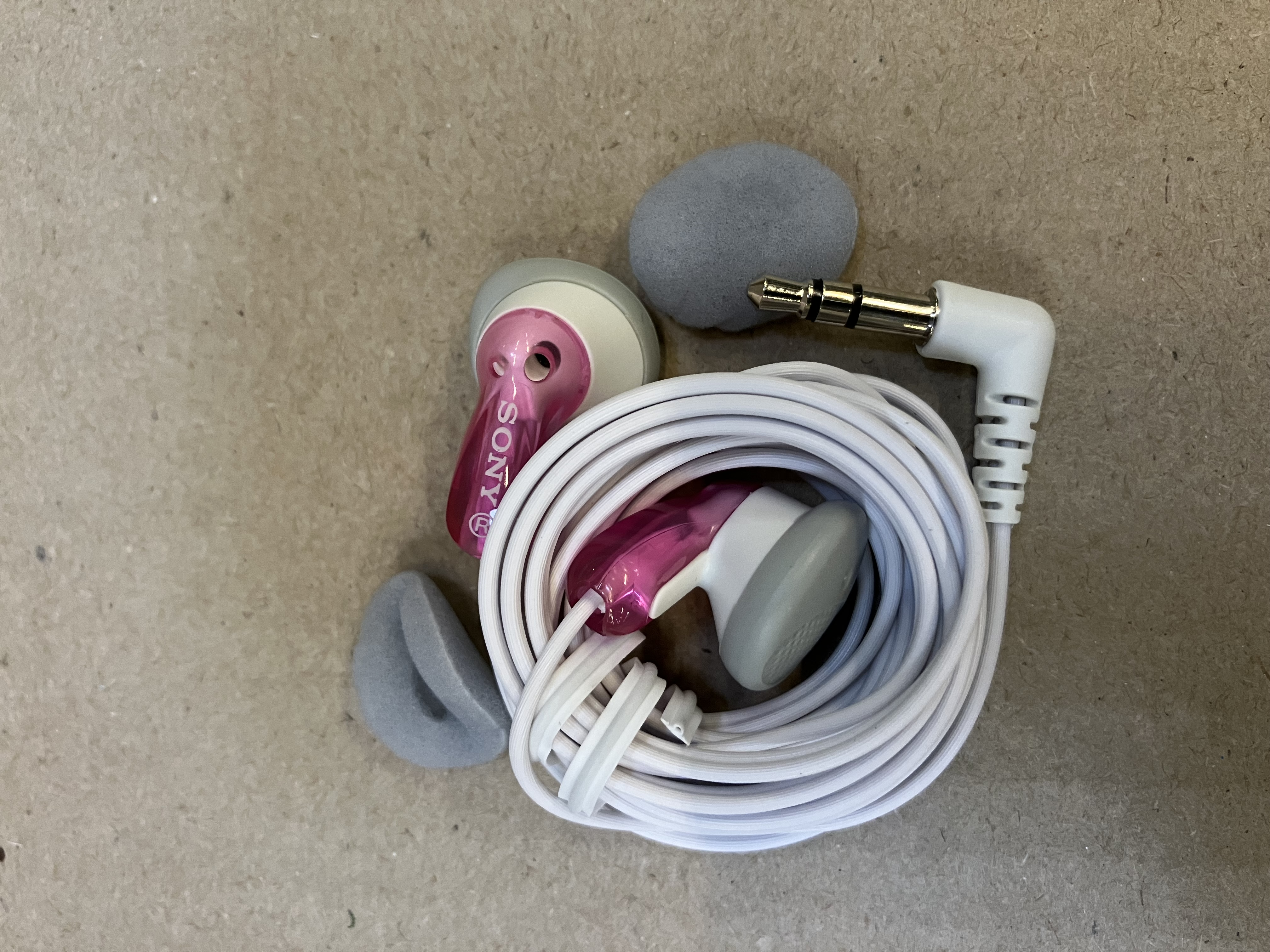 Słuchawki. Różowe i białe słuchawki z białym przewodem i szarymi wkładkami.