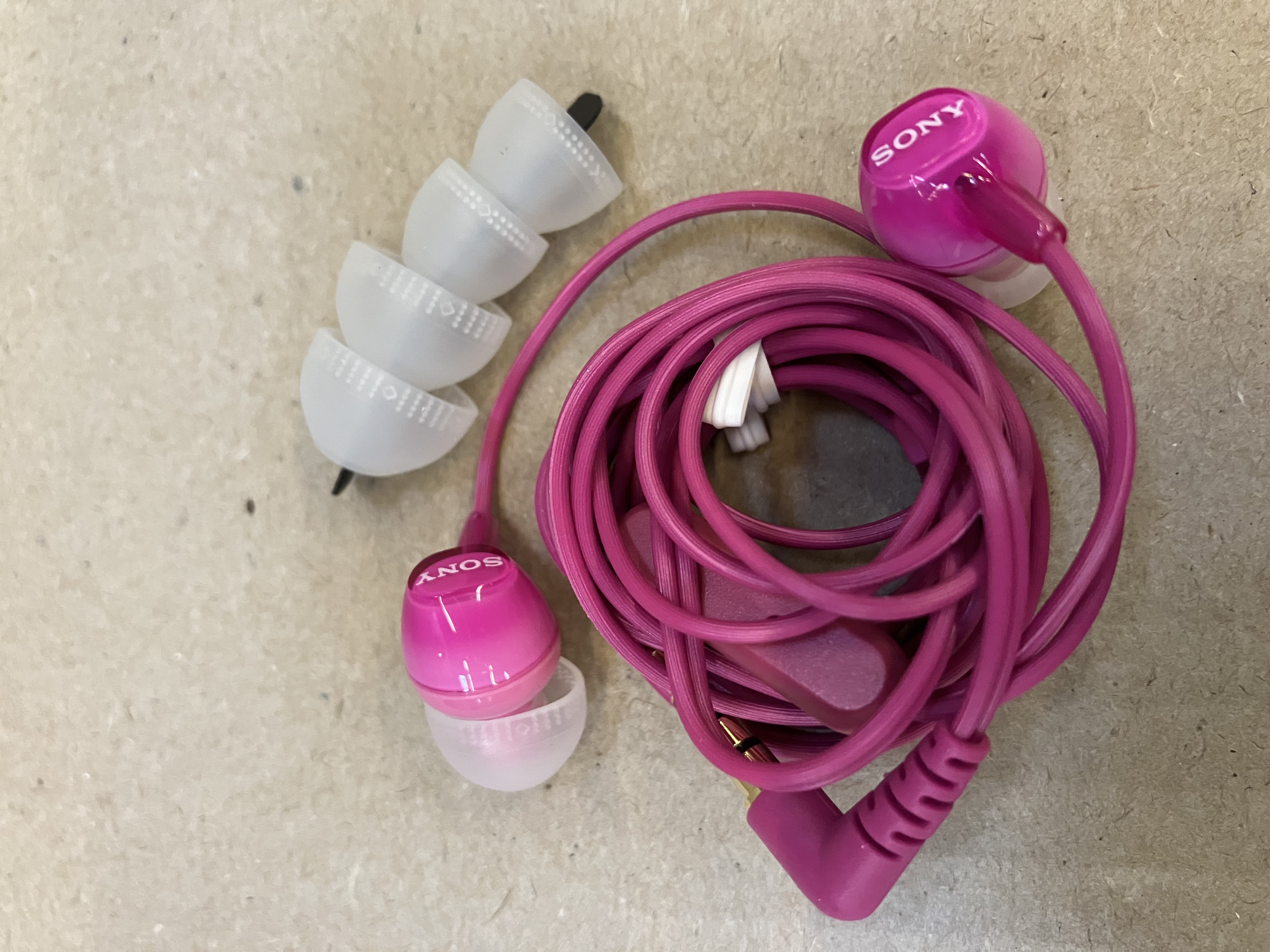 Różowe słuchawki Sony z białymi końcówkami i kablem na jasnym podłożu.