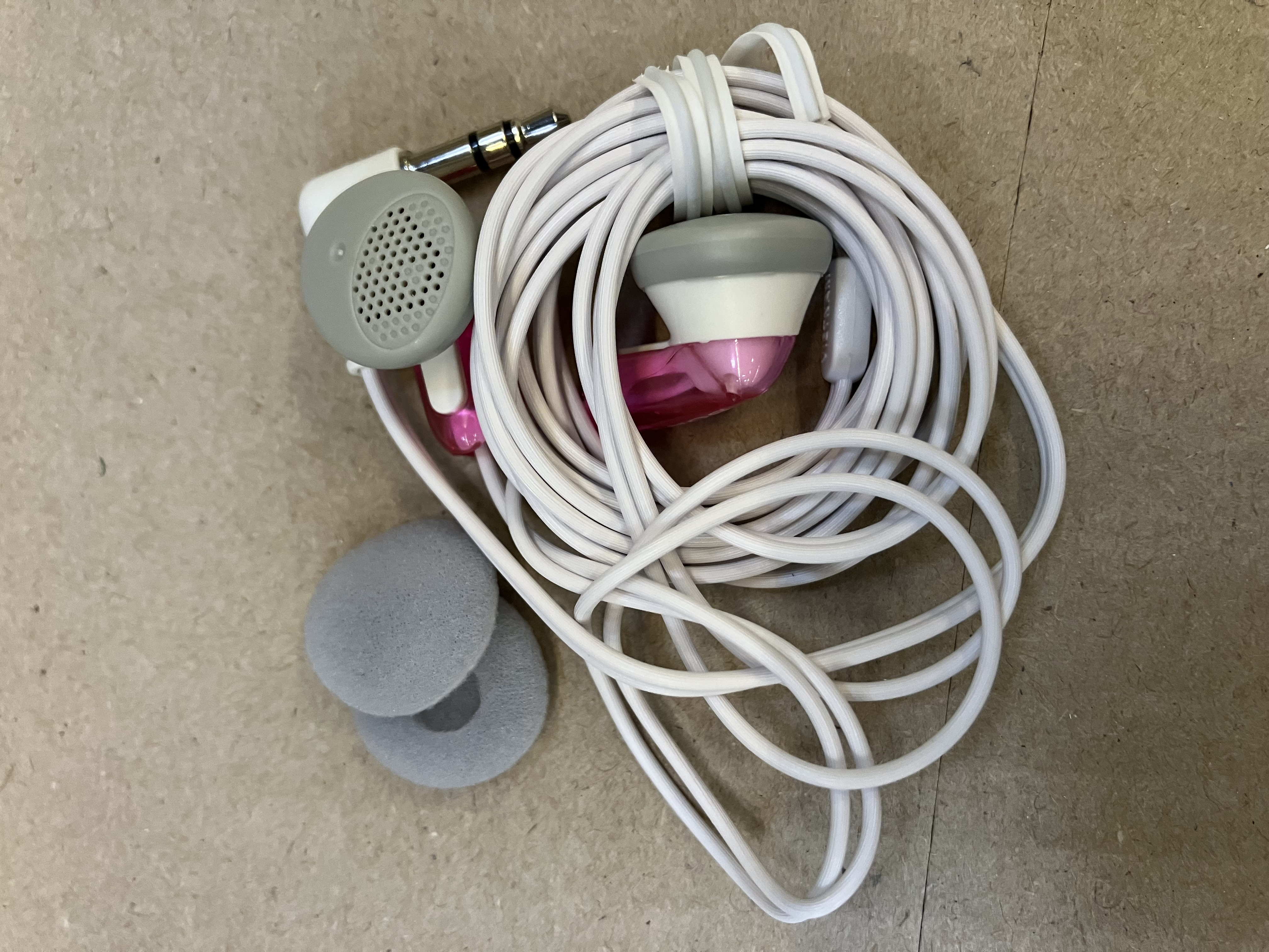 Białe i różowe słuchawki z białym kablem są zwinięte. Obecne są również dwie szare poduszki.