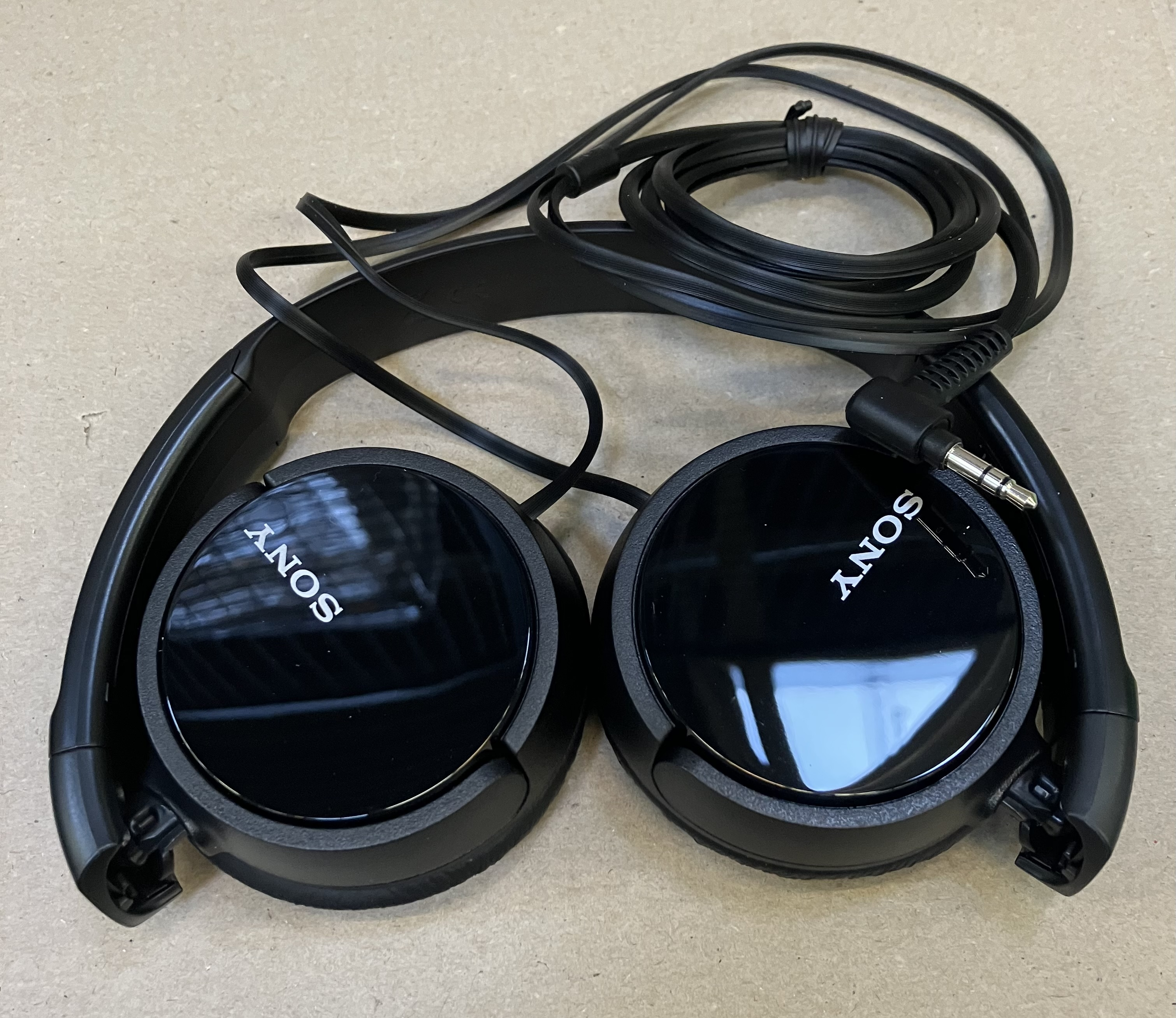 Czarne słuchawki Sony. Słuchawki są rozłożone i leżą na powierzchni. Widoczne jest logo Sony.