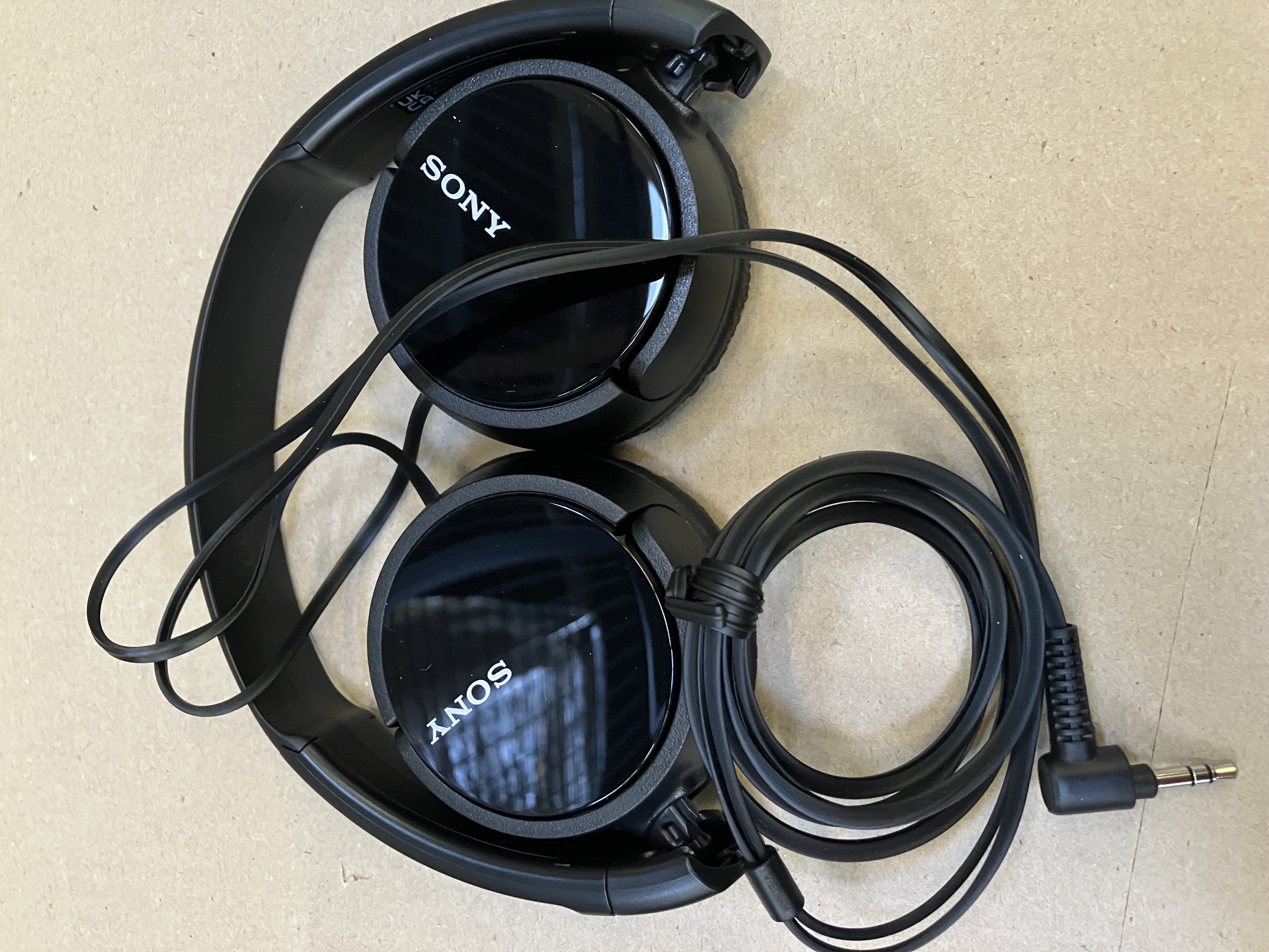 Czarne słuchawki Sony leżące na jasnobrązowej powierzchni z czarnym kablem.