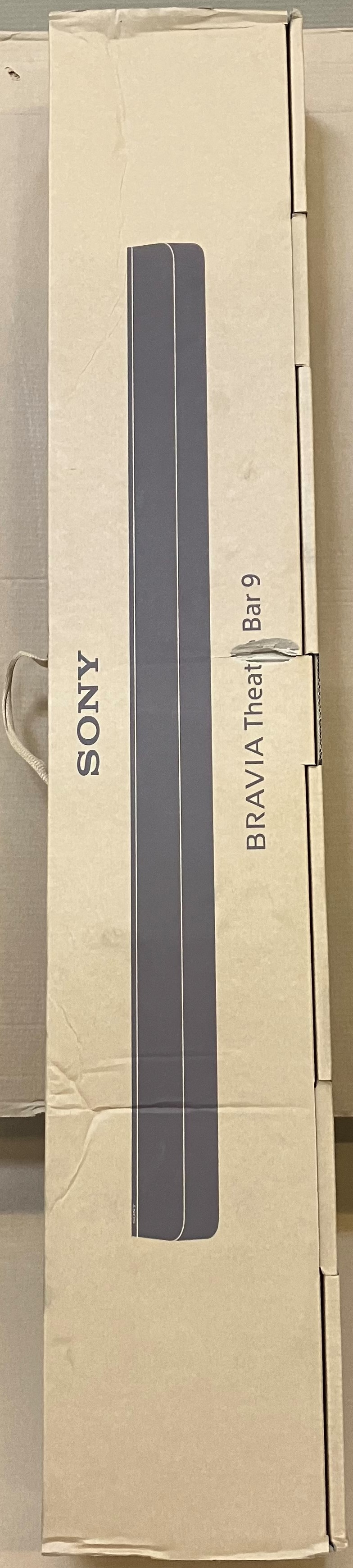Długie, prostokątne pudełko z logo 'SONY'. Pudełko jest jasnobeżowe i ma szary wzór.