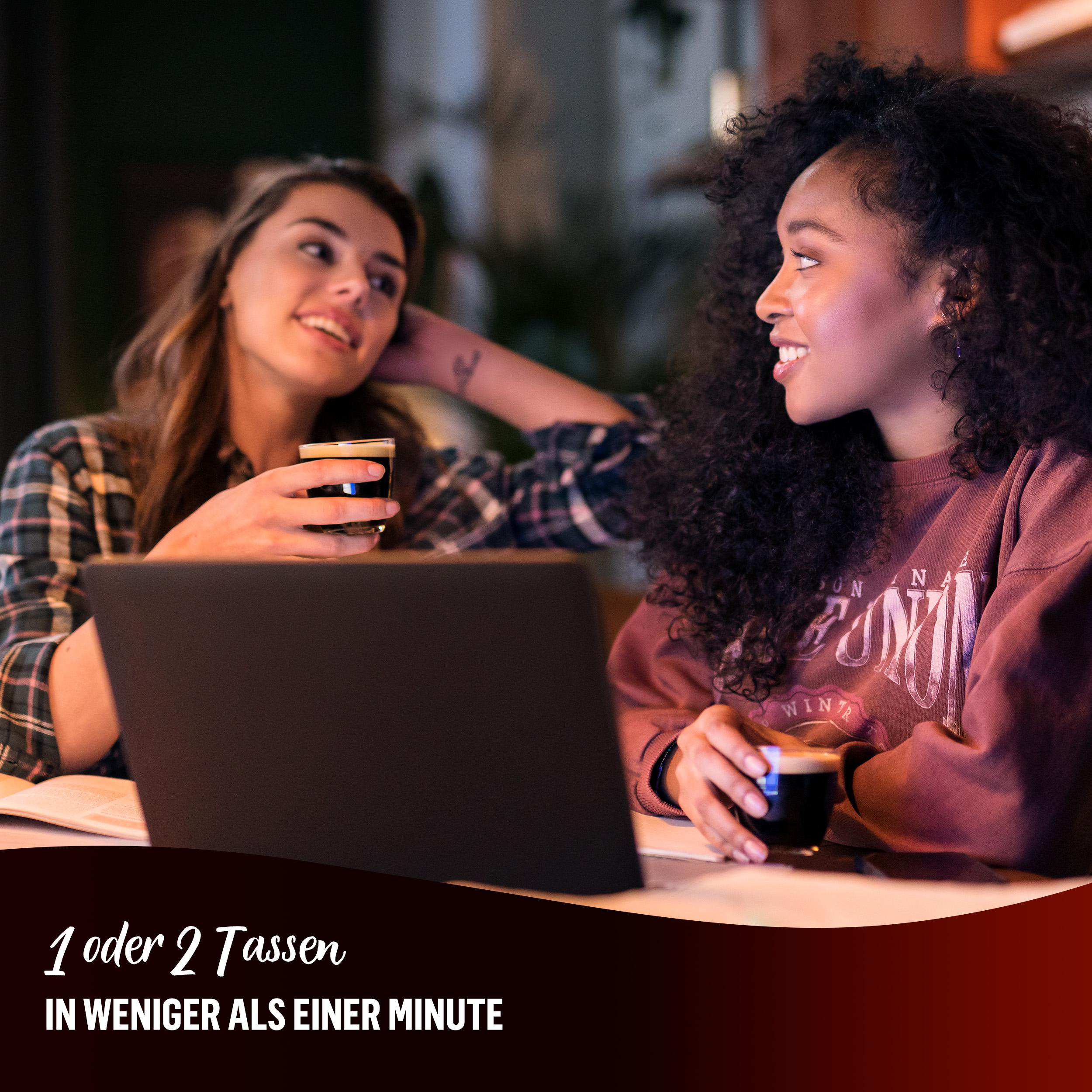 Zwei Frauen in einem Café, eine mit Laptop, trinken dunkle Getränke.