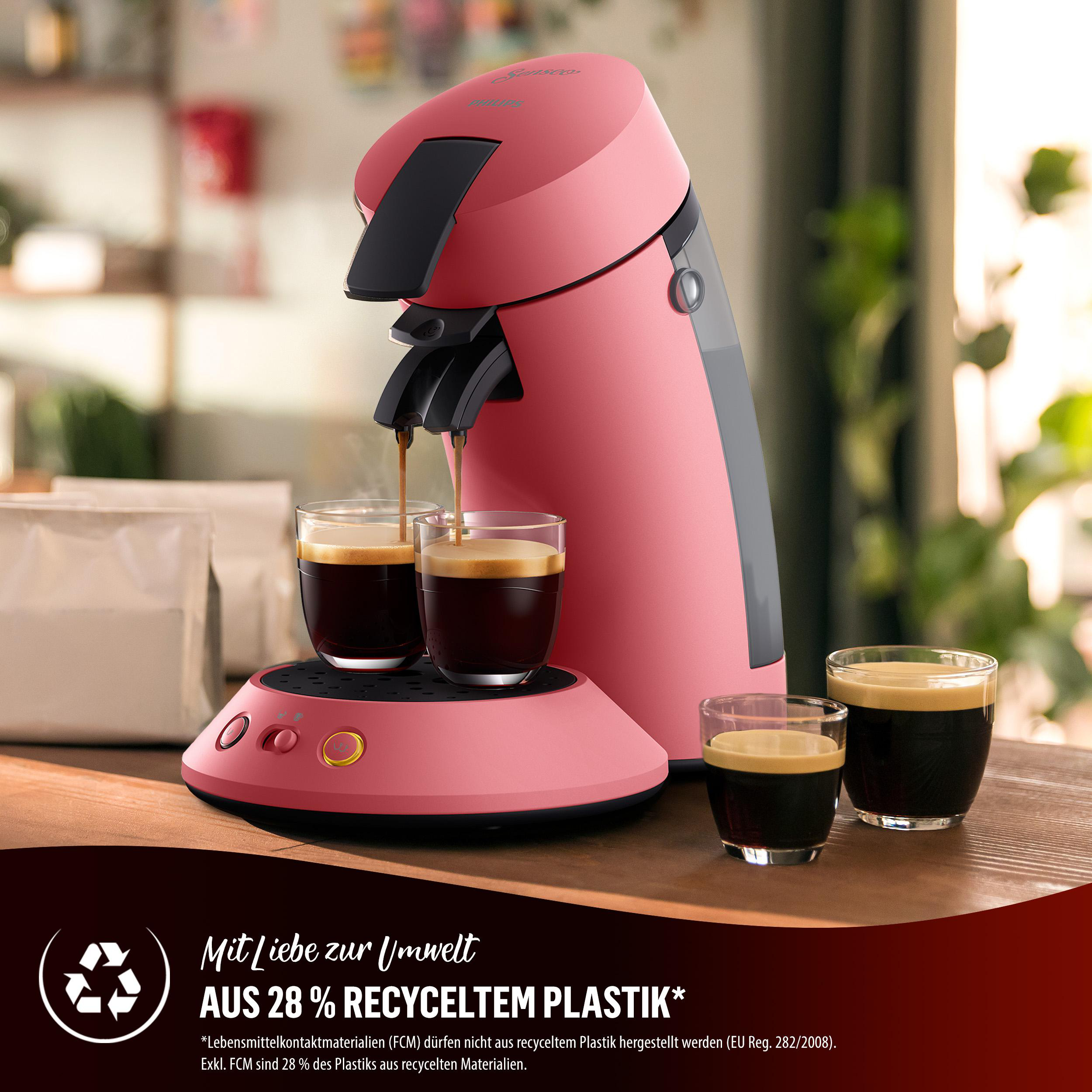 Ein rosa Senseo Kaffeemaschine mit zwei Tassen Kaffee und zwei leeren Gläsern. Auf einem Holztisch.
