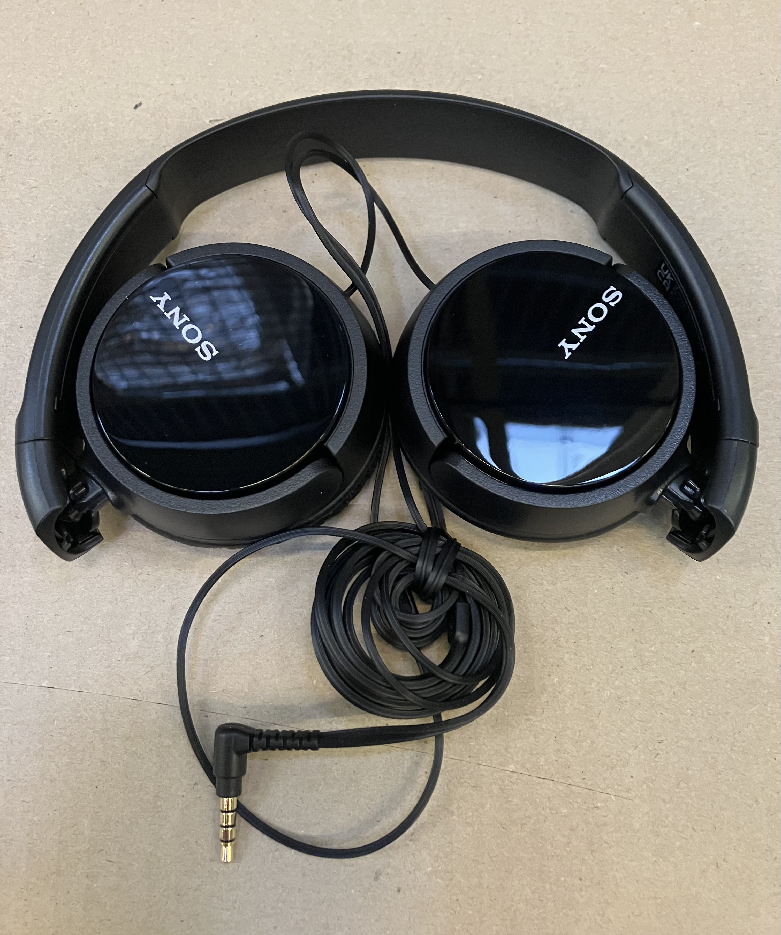 Czarne słuchawki nauszne, zwinięty czarny przewód i złote złącze na powierzchni.