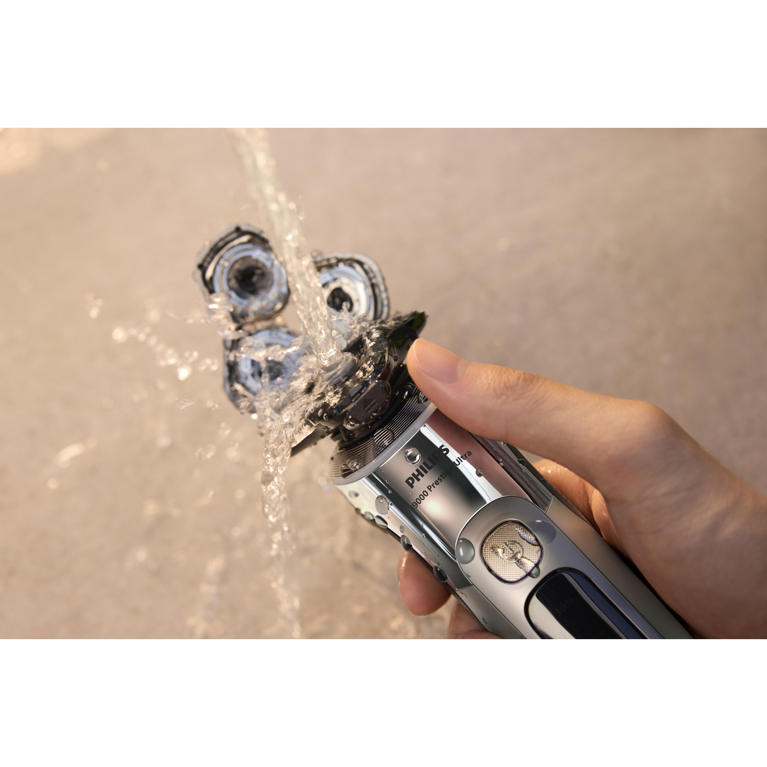 A hand holds a silver shaver under running water, washing it.