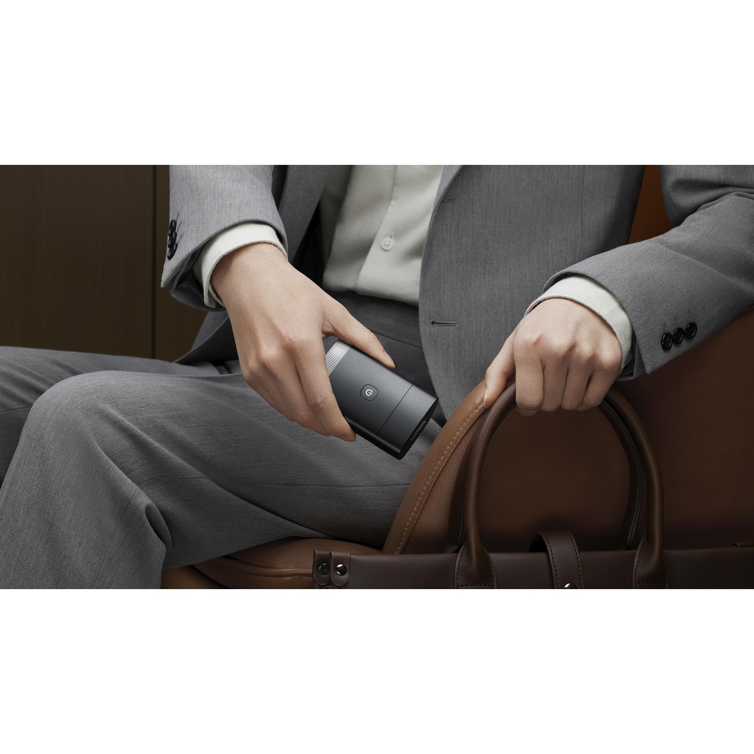 Person in grey suit holding a black grooming device in a brown leather bag.