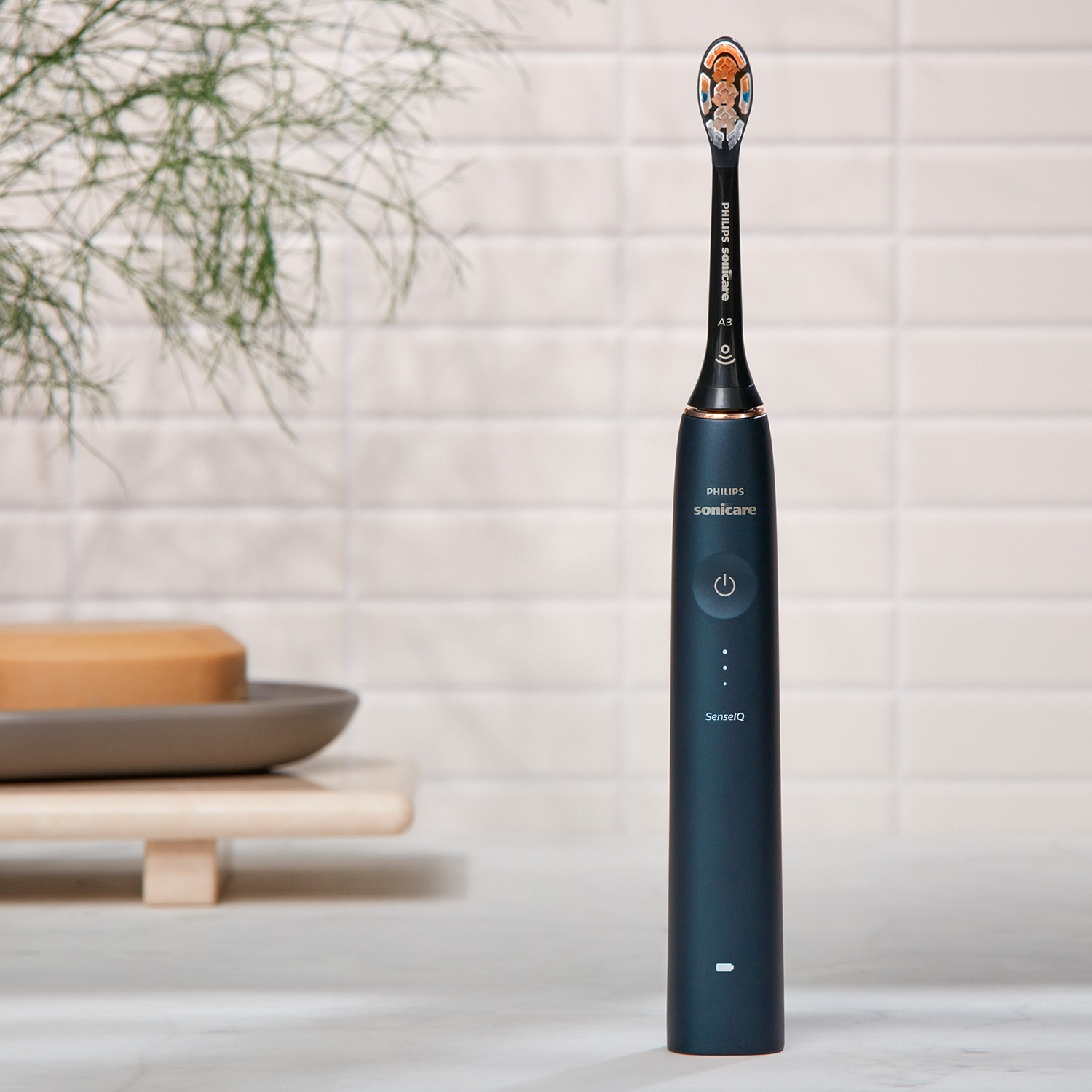 Brosse à dents électrique noire, accents bleus, sur une surface en marbre. Savon et plante en arrière-plan.