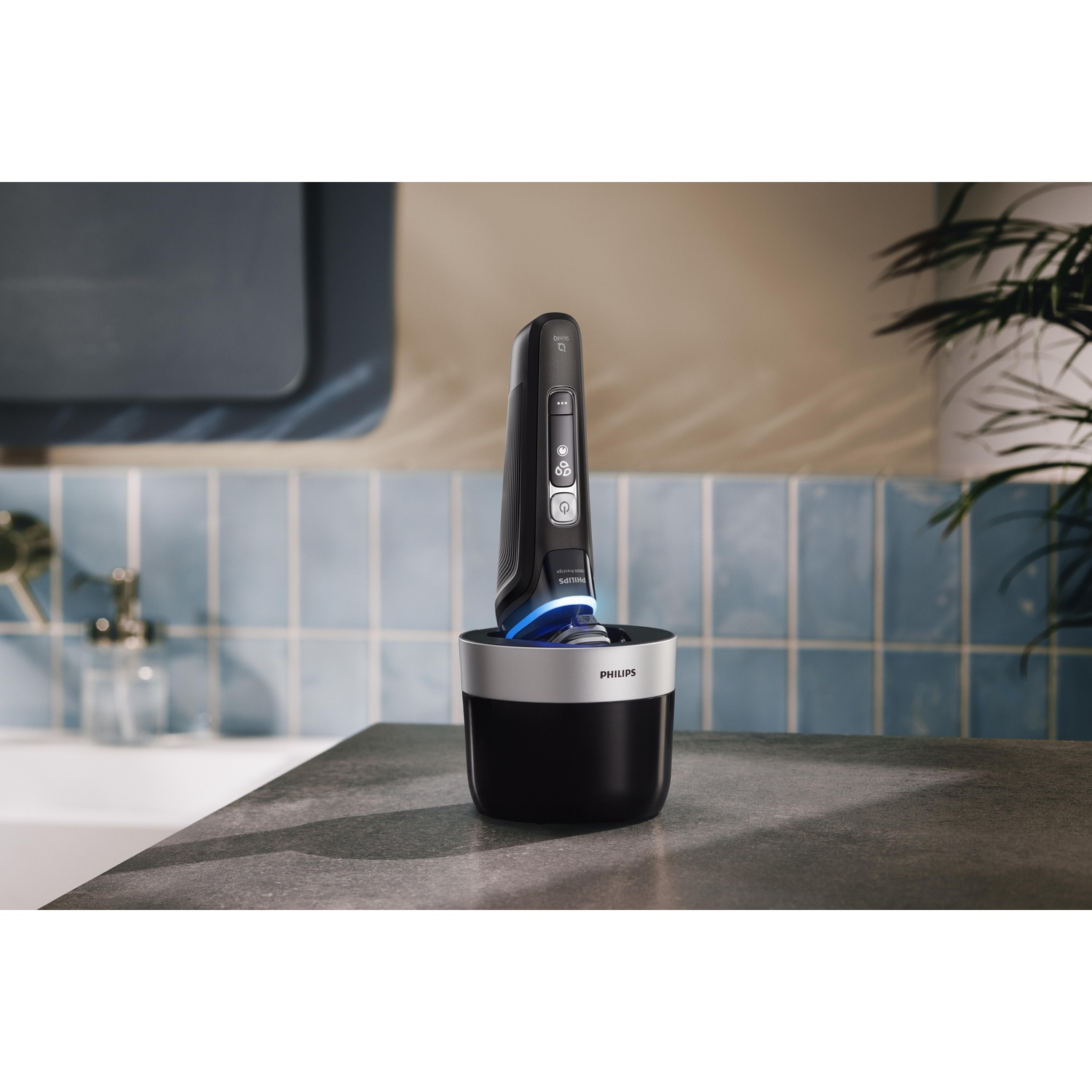 Un rasoir électrique noir est dans une base de charge noire. La scène est une salle de bain avec des carreaux bleus.