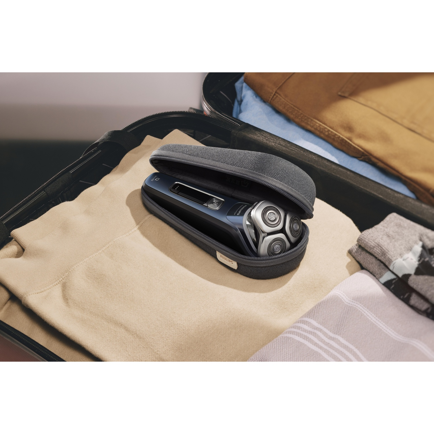 Elektrisch scheerapparaat in een etui in een open koffer met kleding.