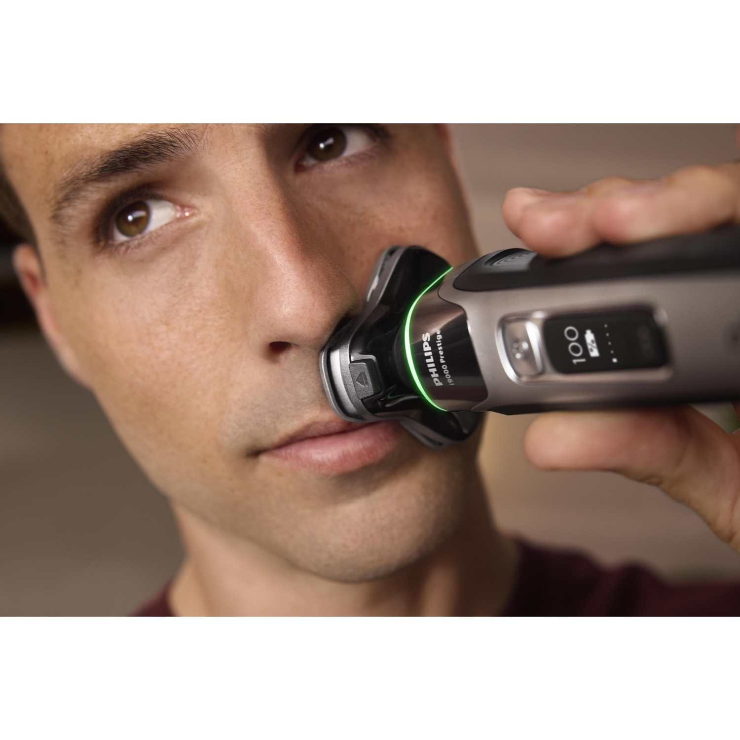 Man shaving his face with a Philips shaver; green light and number 100 are visible.
