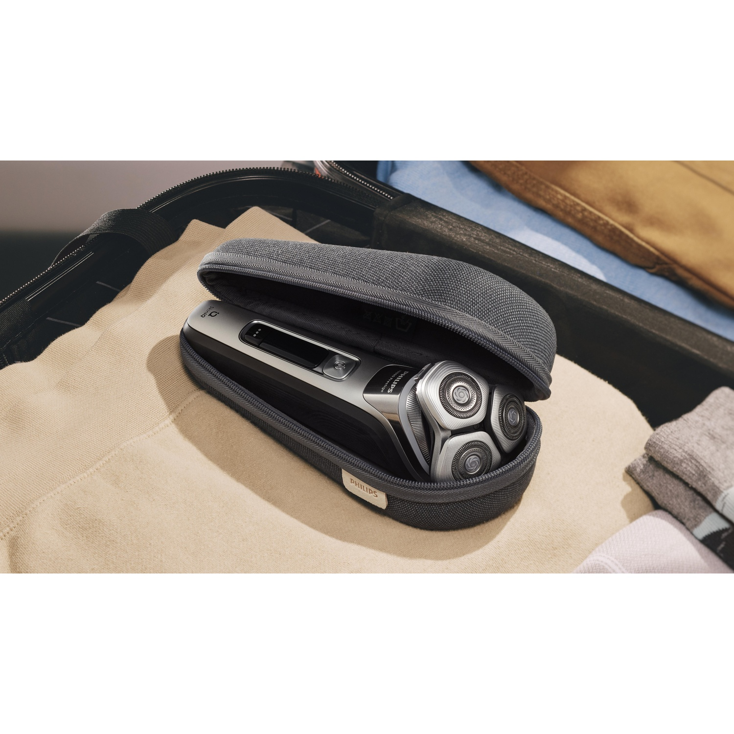 Silver and black electric shaver in a gray case, lying on a tan surface.