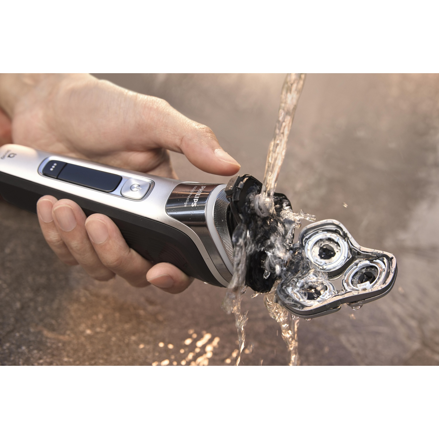 A person shaving with a silver and black electric razor under running water.