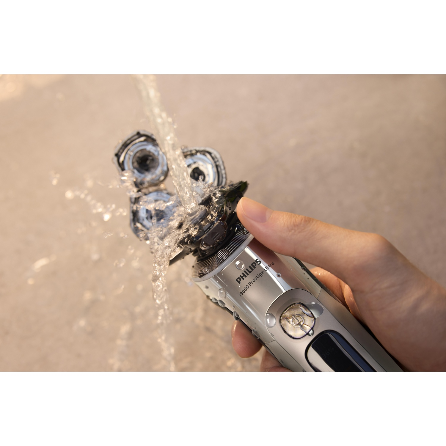 A hand holds a black shaver under running water, washing it.