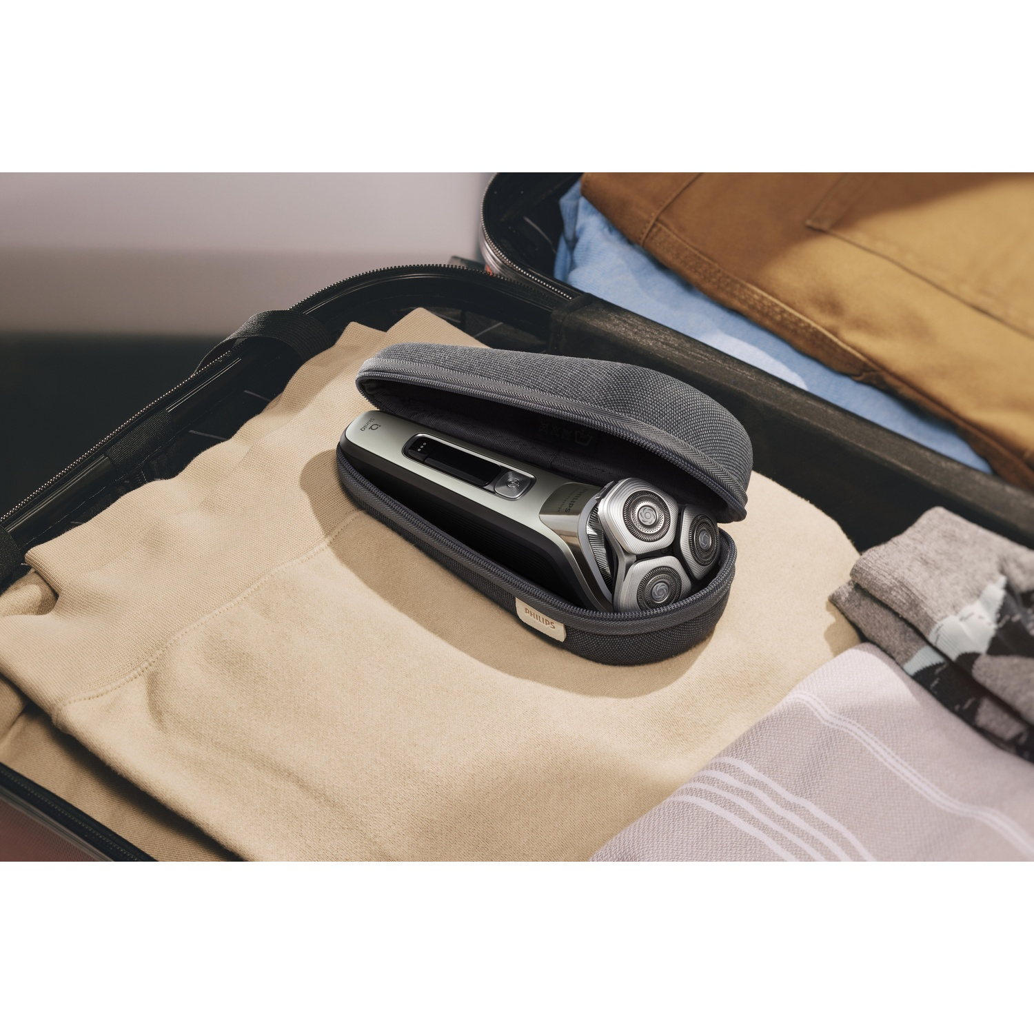 A Philips shaver in a travel case. The case is open, revealing the shaver and accessories on a beige surface.