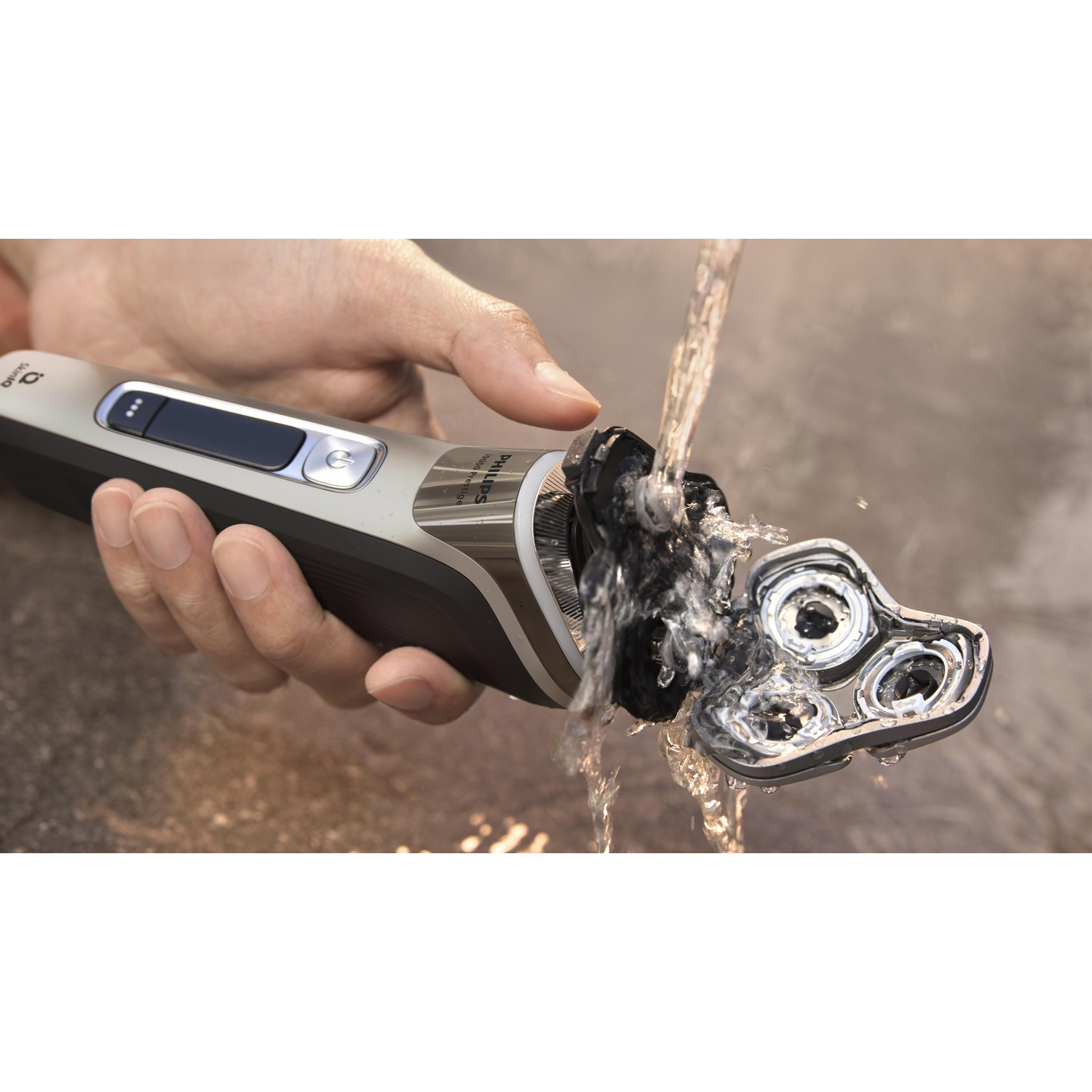 A hand holding a Philips shaver under running water. The shaver is open and being rinsed.