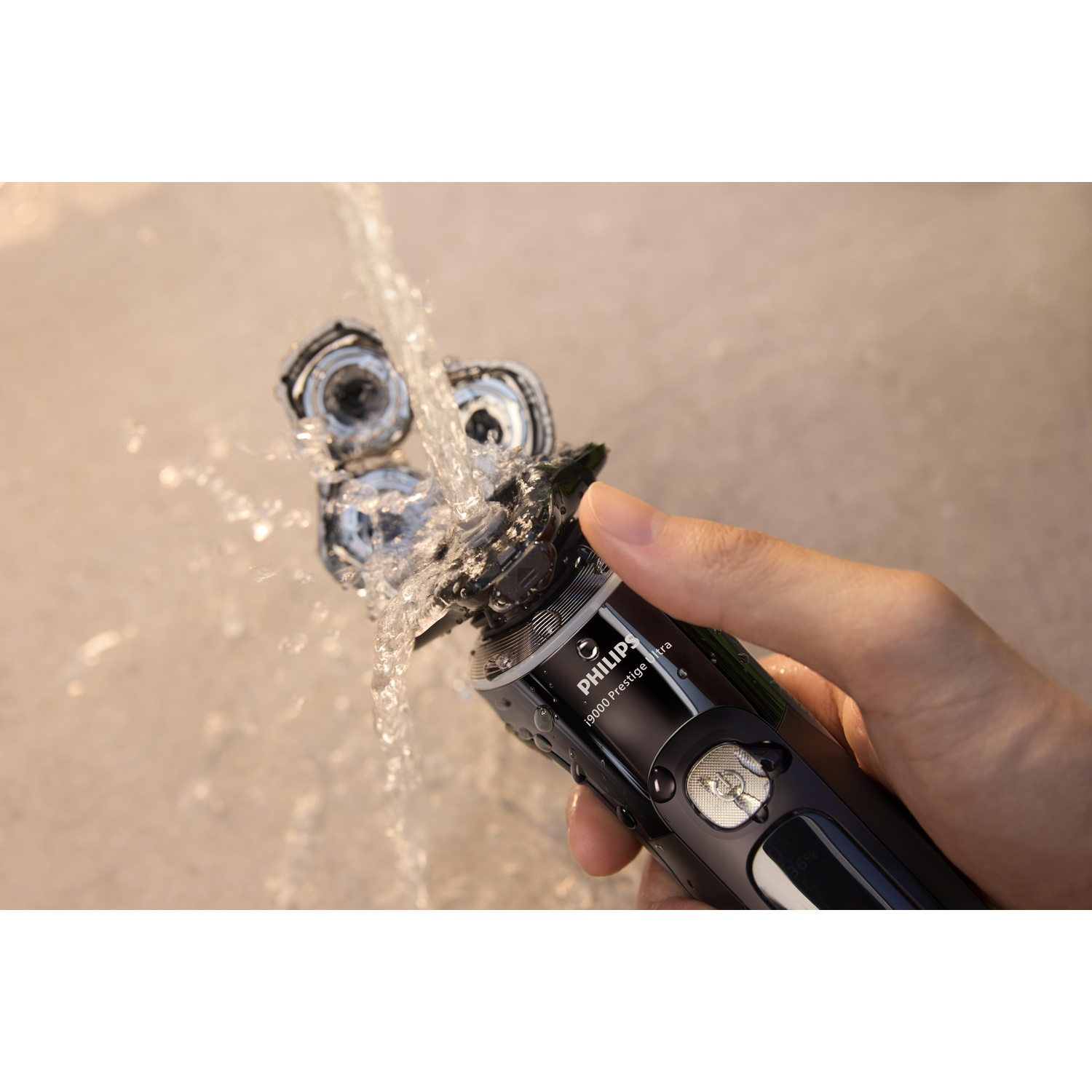 A hand holds a black and silver Philips electric shaver under running water.