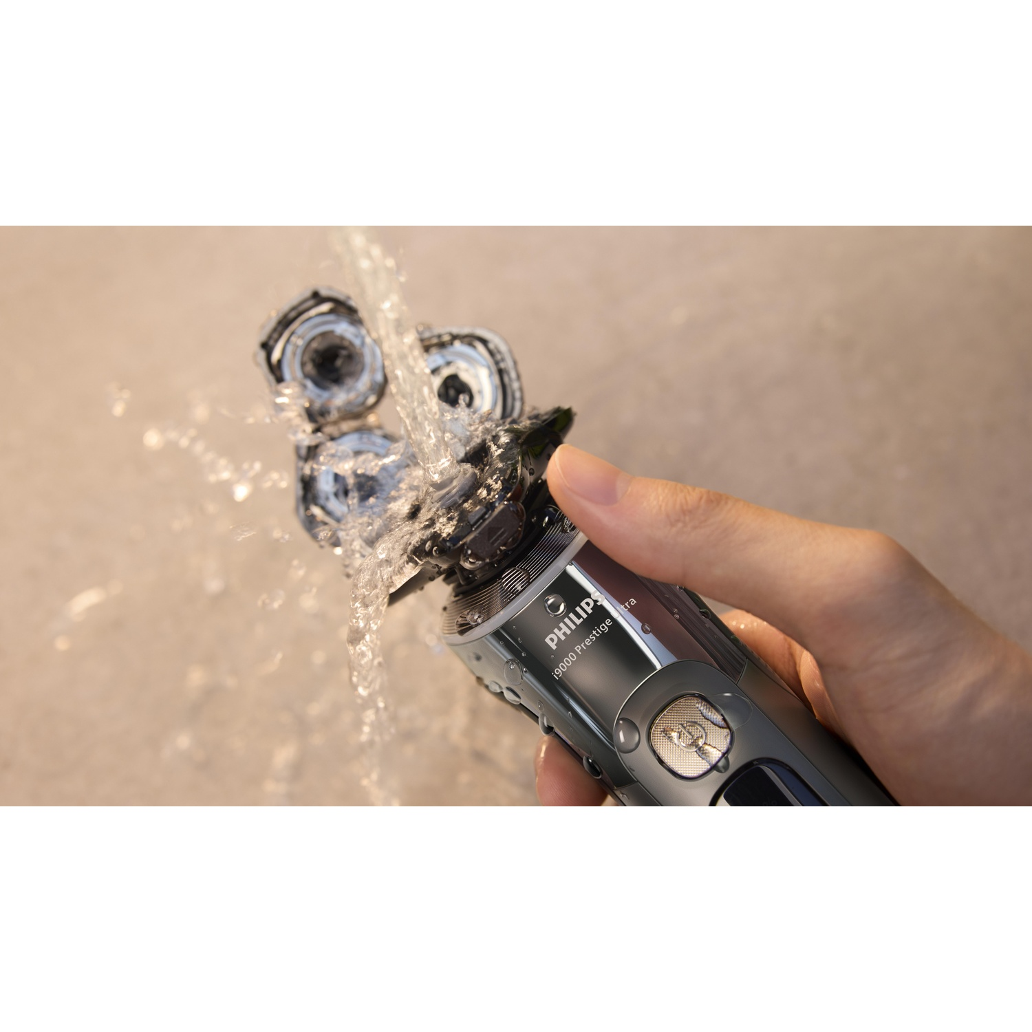 Hand holding electric shaver under running water, silver shaver.