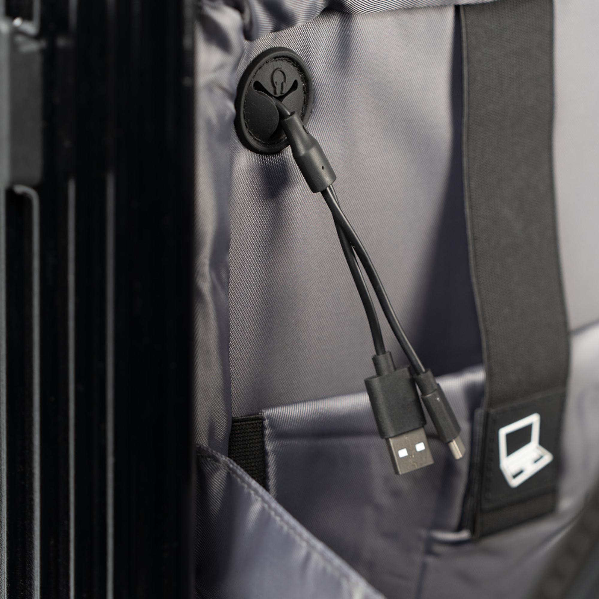 Nahaufnahme des Rucksackinneren mit einem schwarzen USB-Kabel und einem Laptop-Symbol. Grauer Stoff.
