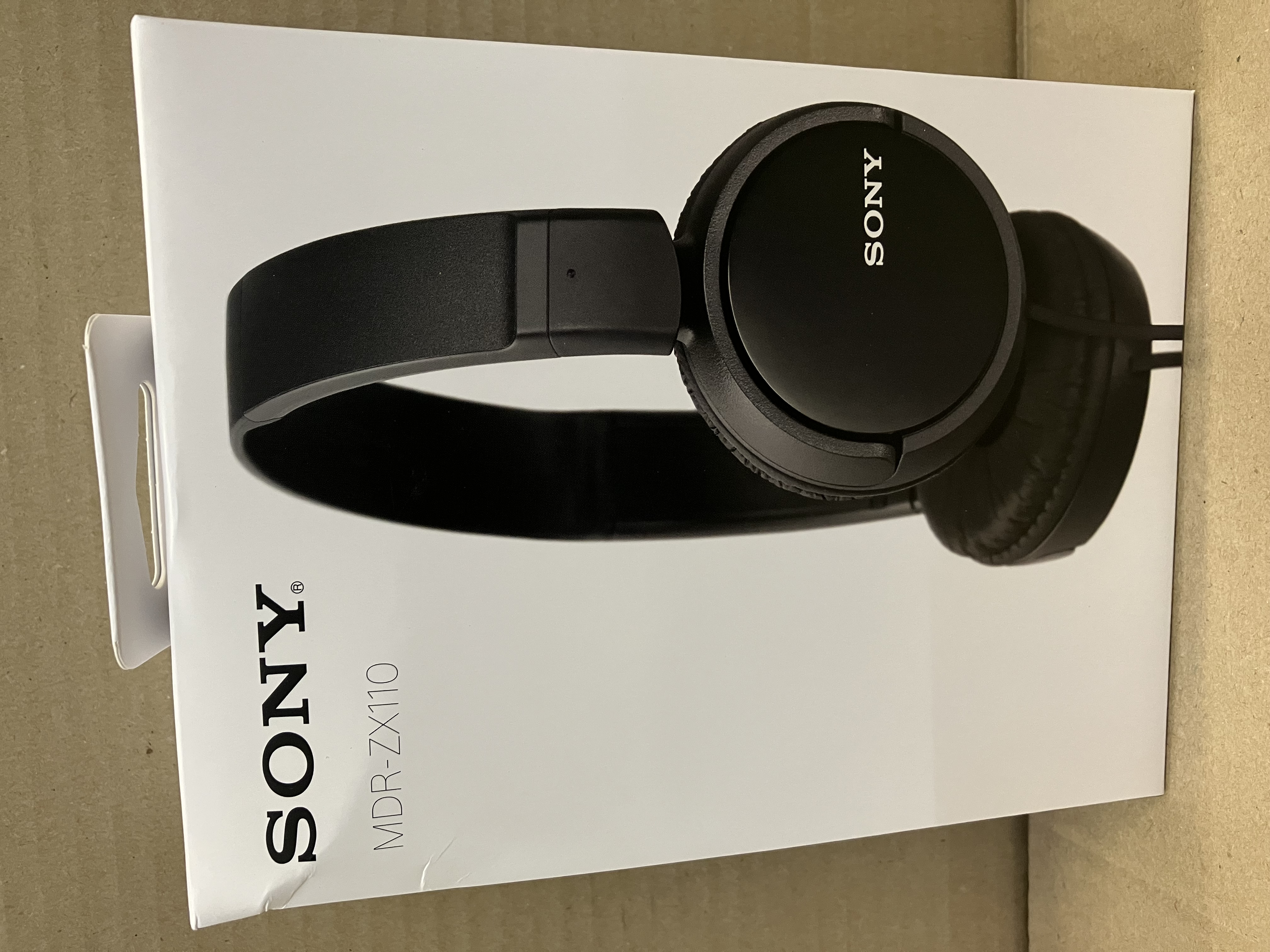Czarne słuchawki na białym pudełku z napisem "SONY". Słuchawki są skierowane w prawo.