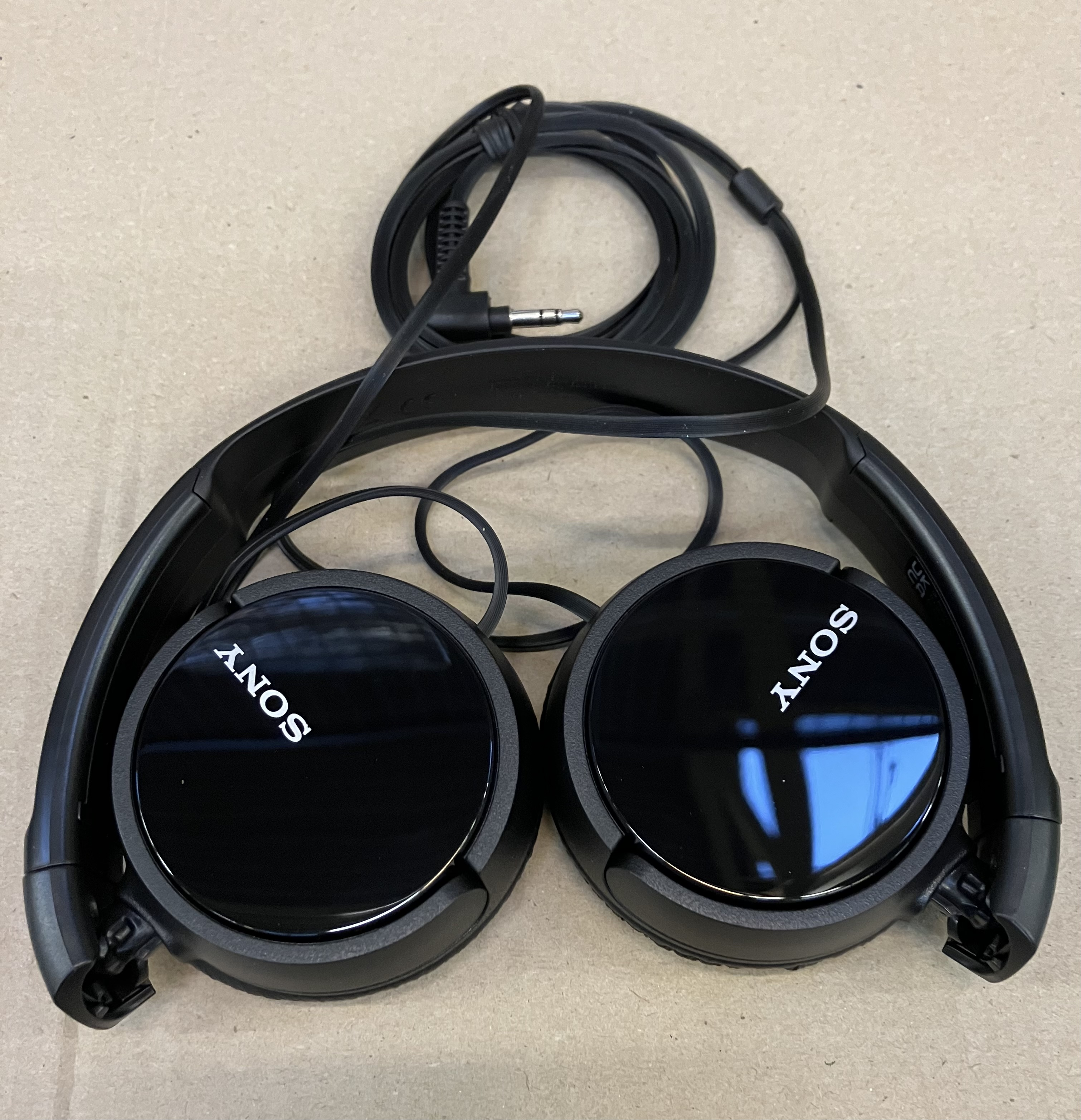 Czarne słuchawki Sony z nausznikami i czarnym kablem na brązowej powierzchni.