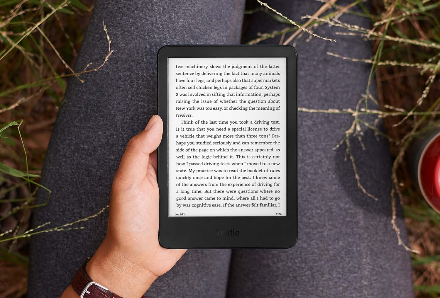 Egy személy kezei egy Kindle e-olvasót tartanak, a képernyőn egy könyvvel.