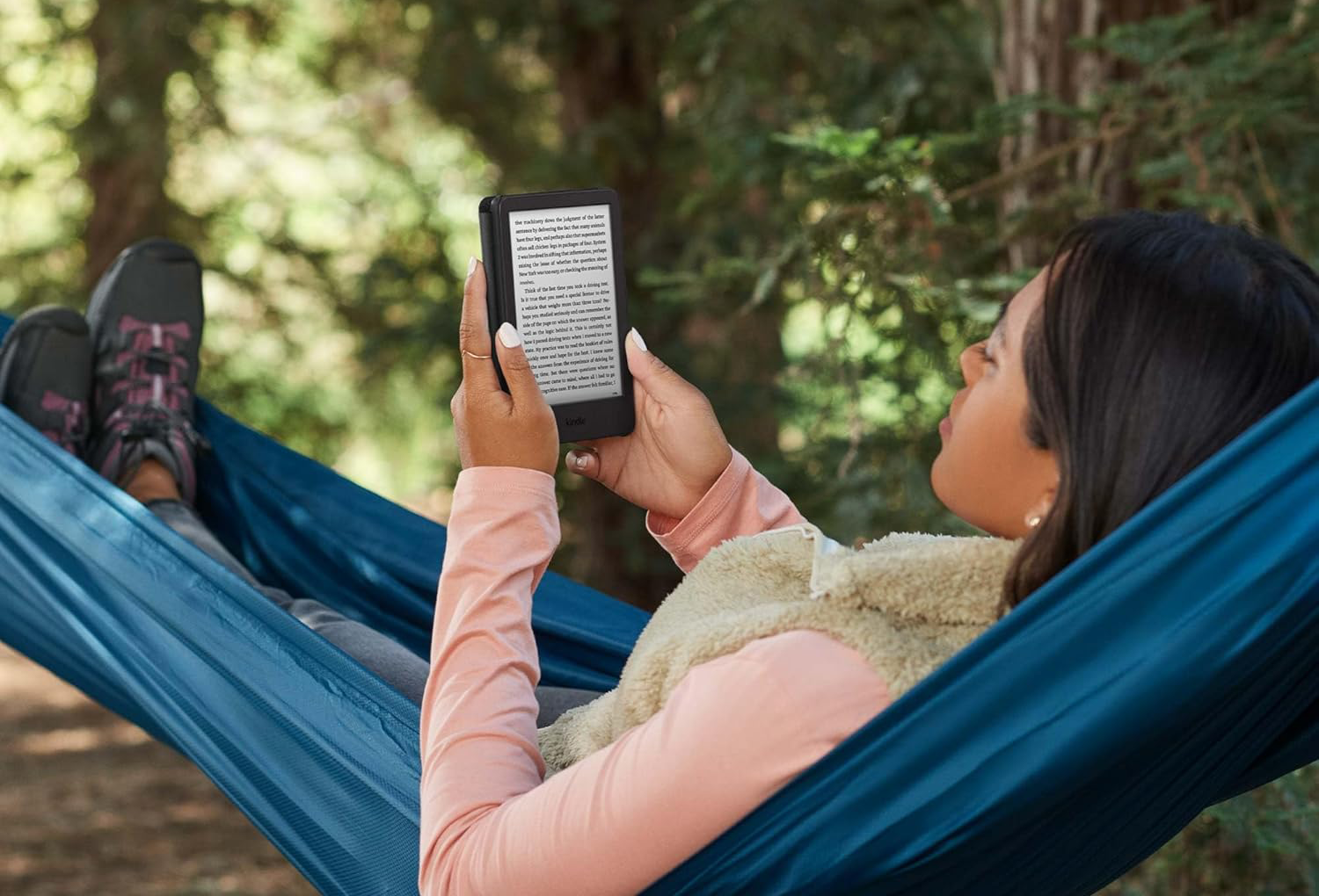 Nő Kindle-t olvas egy függőágyban pihenve. Fák a háttérben.