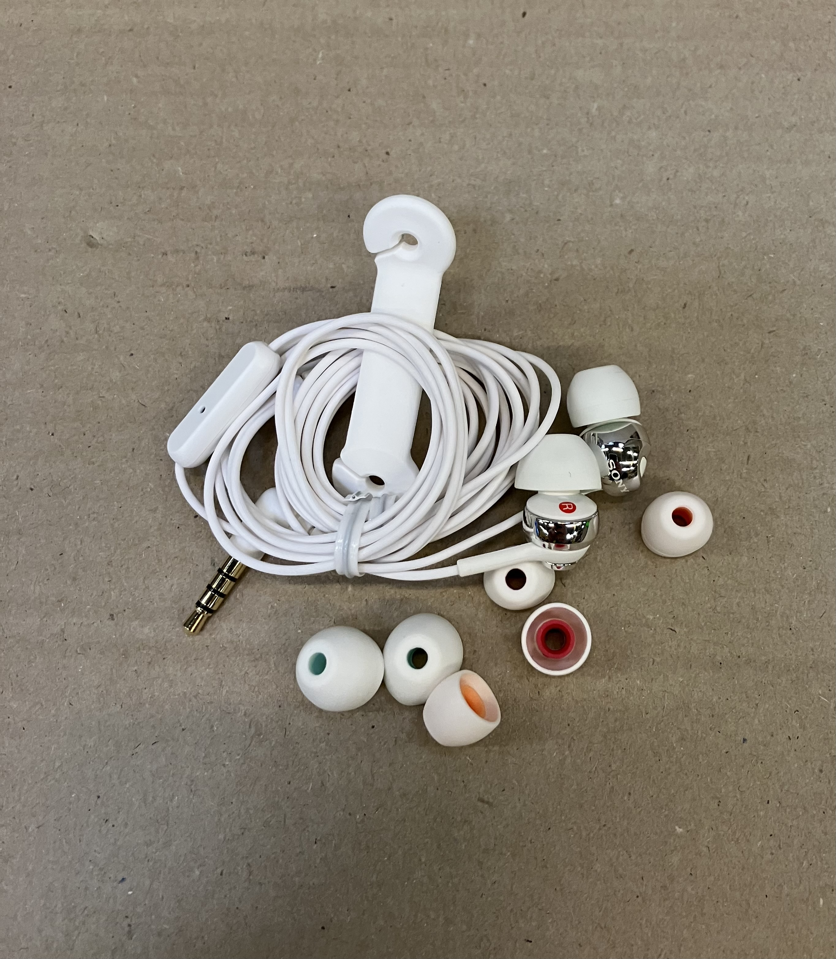 Białe słuchawki, kabel i akcesoria na brązowej powierzchni.