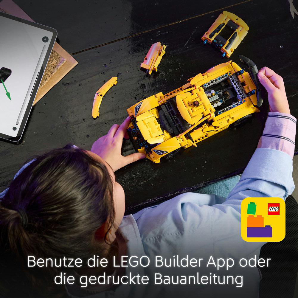 Eine Person baut ein gelbes Lego-Auto mit Teilen. Tablet auf dem Schreibtisch.