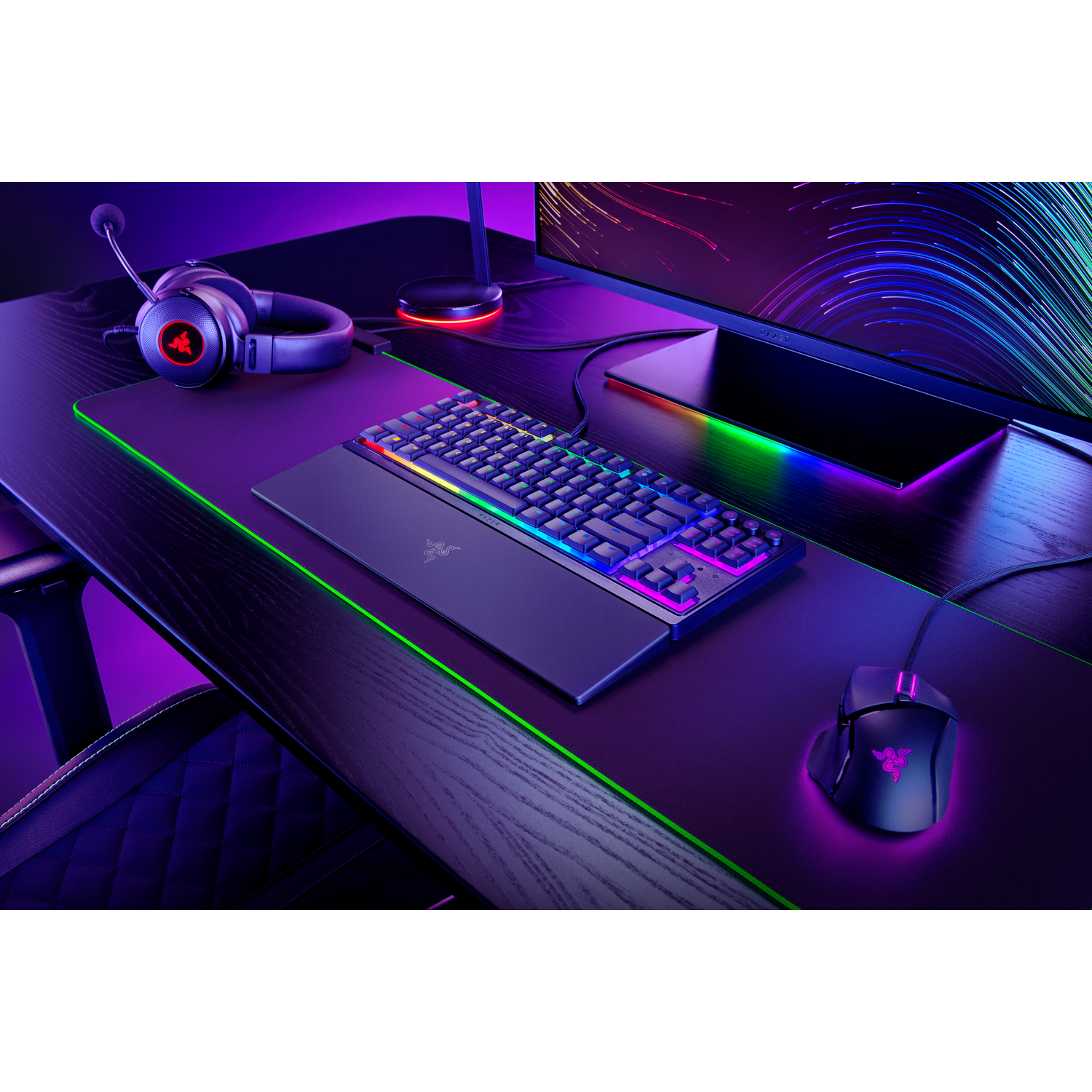 Gaming setup with keyboard, mouse, headset, and monitor on a desk, with colored lights.