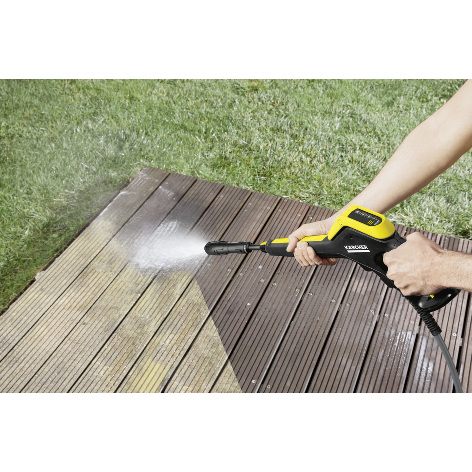Personne pulvérisant de l'eau sur une terrasse en bois avec un nettoyeur haute pression.