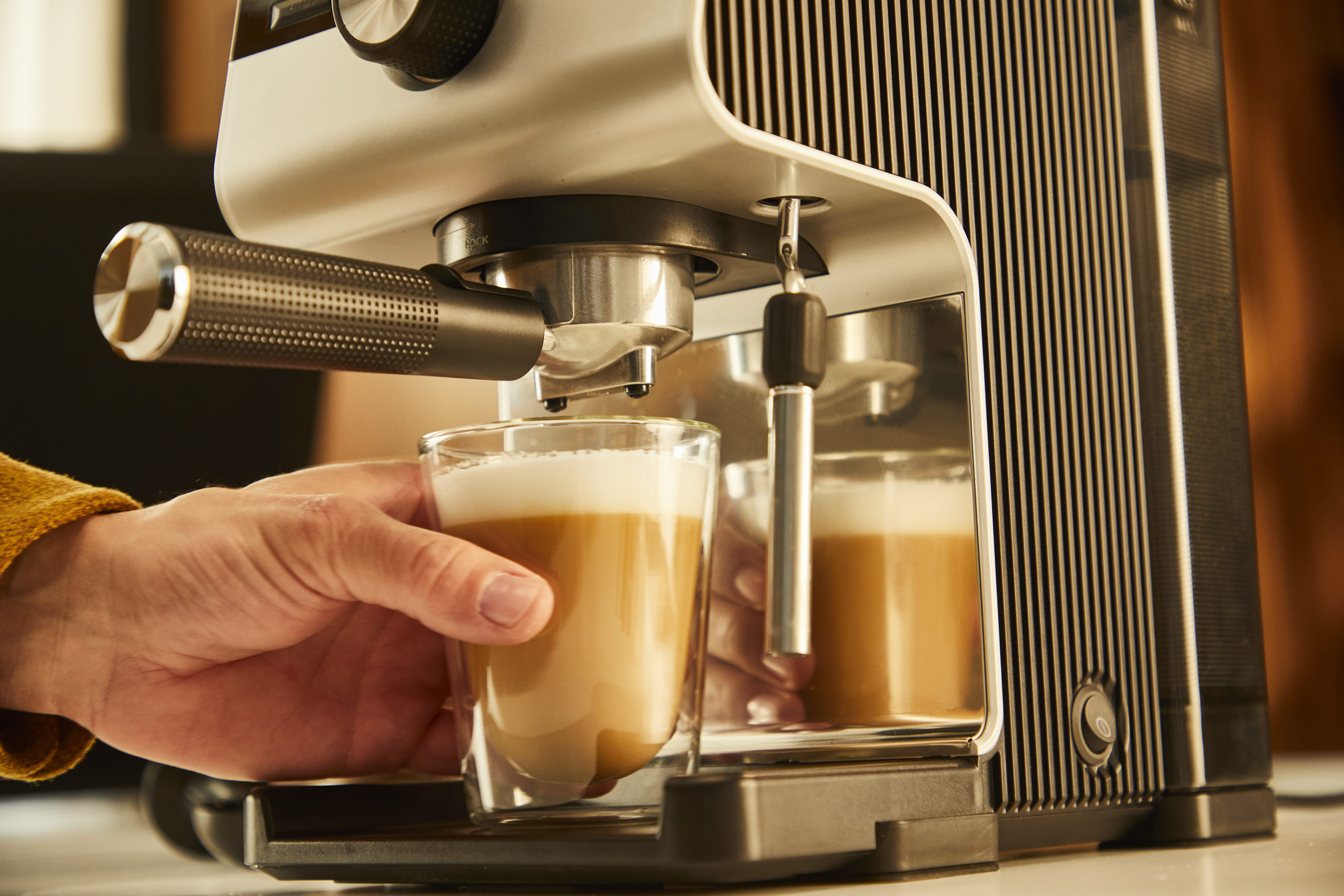 Ręka trzymająca szklankę latte z ekspresu do kawy w czarno-białym designie.