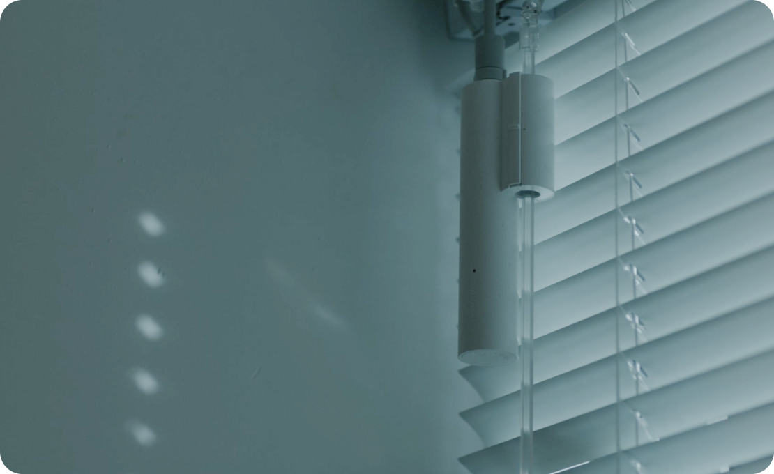 Nahaufnahme eines weißen Jalousienmechanismus und Jalousien. Schatten und Licht spielen an der Wand.