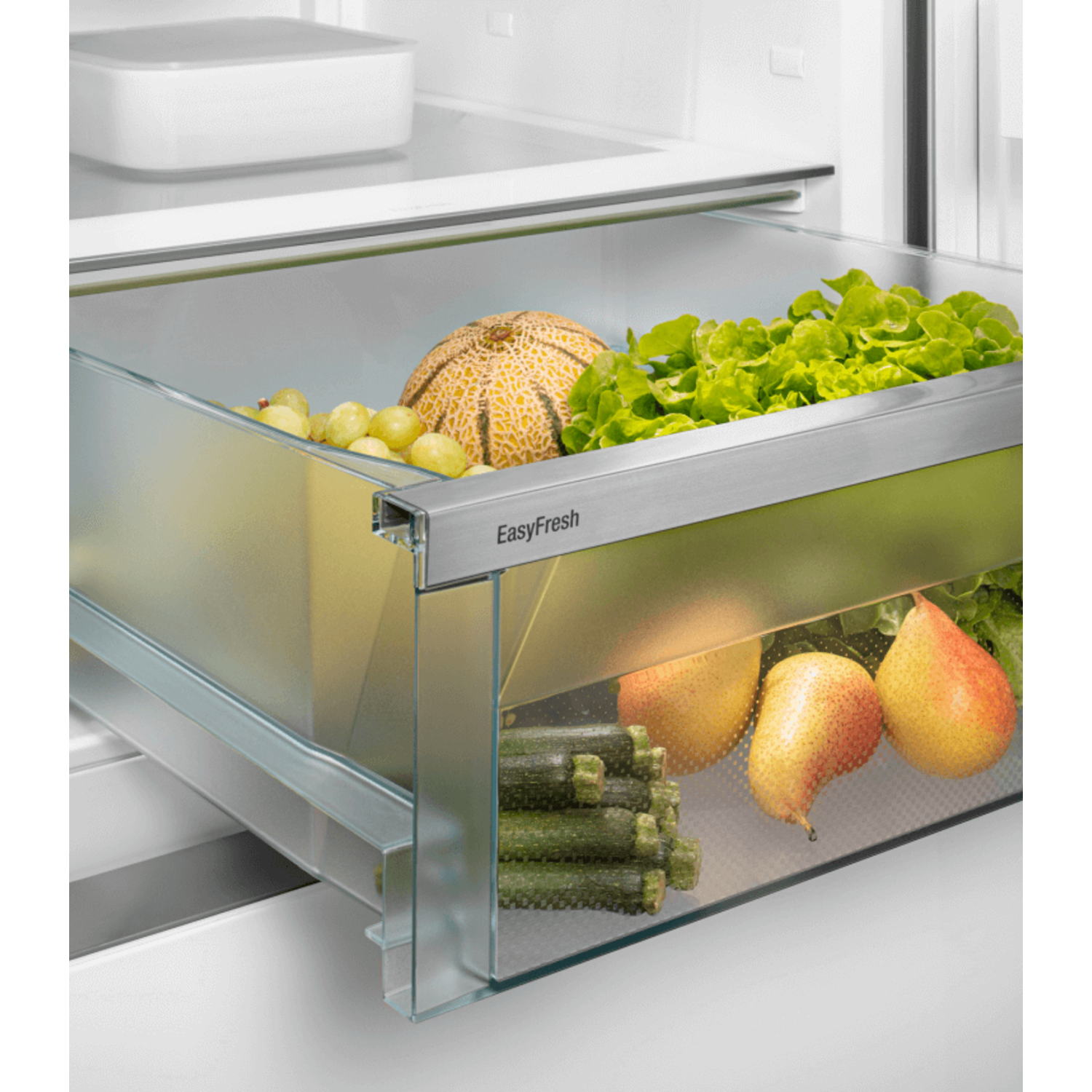 Refrigerator drawer filled with fresh produce: melon, grapes, lettuce, zucchini, and pears.