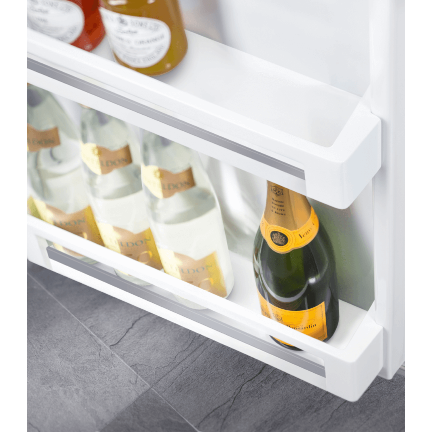 Inside a refrigerator, three bottles of white wine and one of champagne are in a shelf.