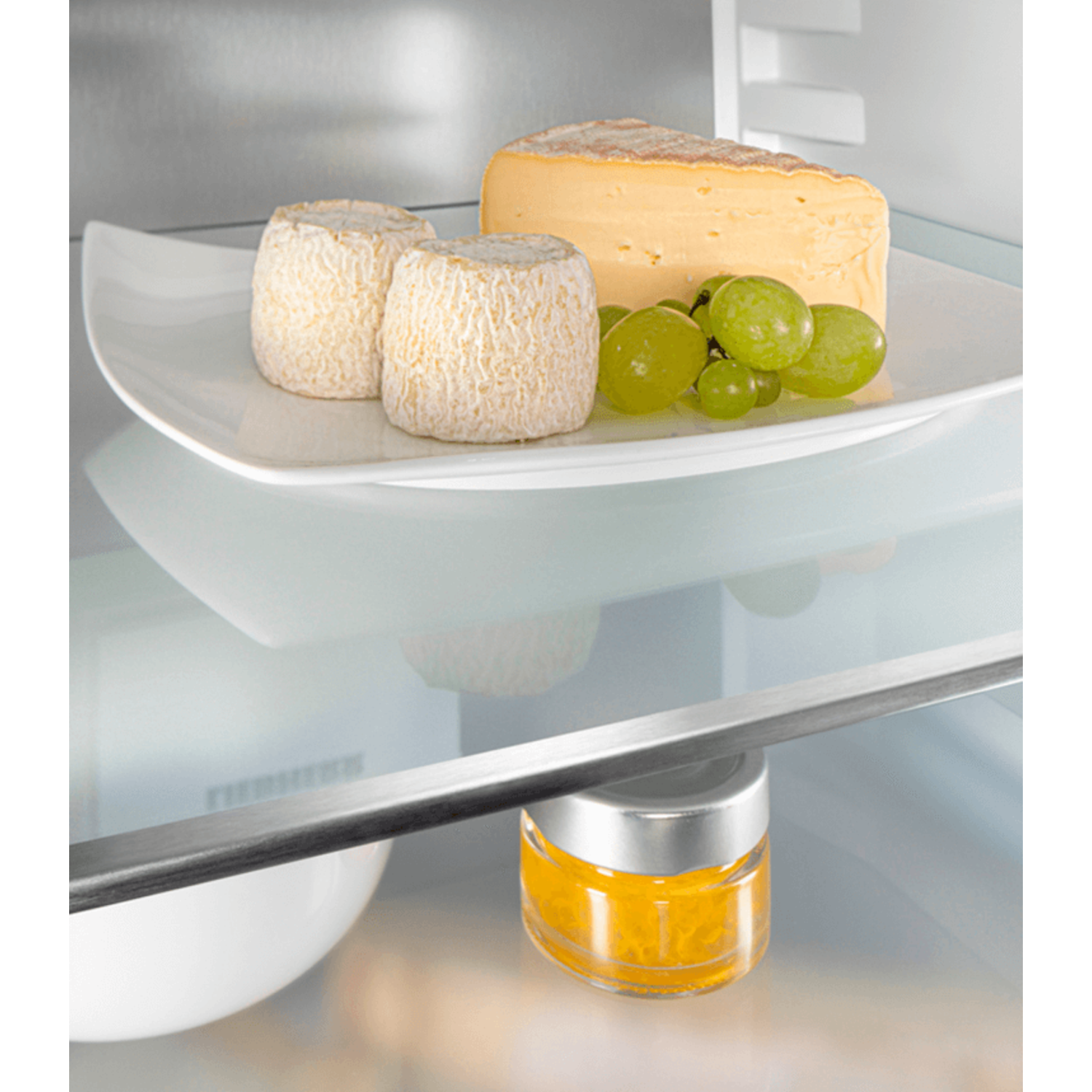 Cheese and grapes on a white plate in a refrigerator.