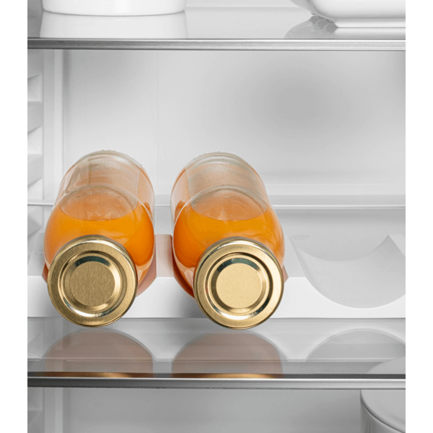 Two glass bottles of orange juice lying on a shelf in a refrigerator.
