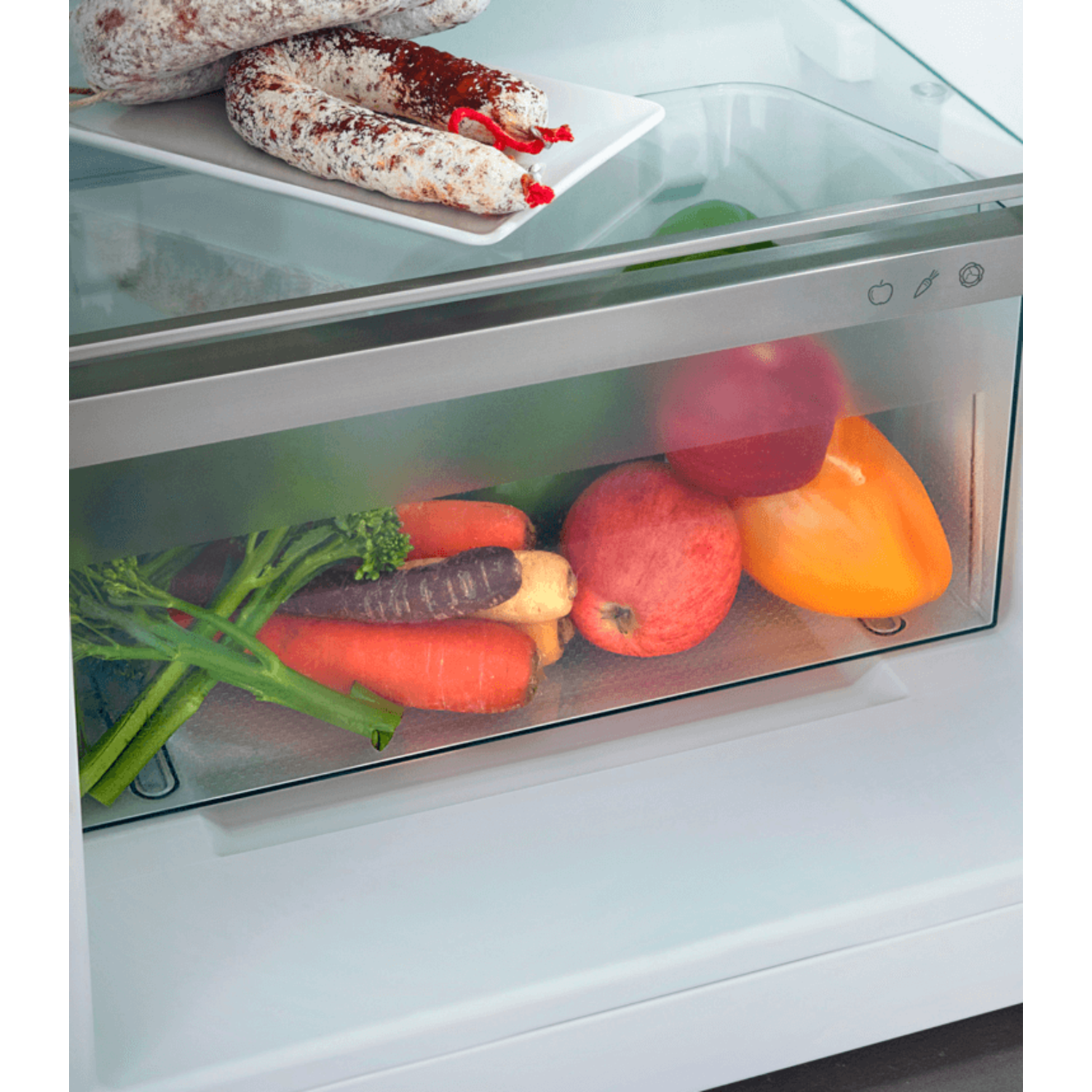 Fridge interior with vegetables, fruit, and sausage. Carrots, apples, and peppers are in a drawer.