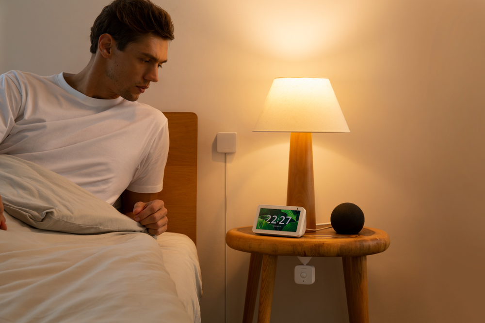 Mann blickt auf einen Smartscreen auf einem Holztisch neben einer Lampe.