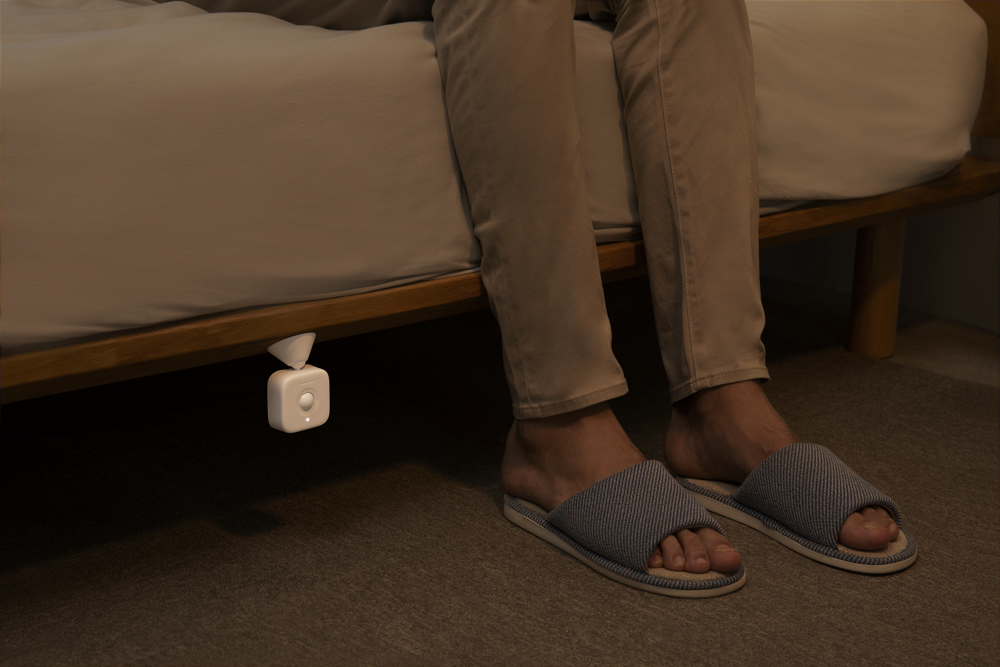 Füße einer Person in der Nähe eines intelligenten Nachtlichts unter einem Bett.