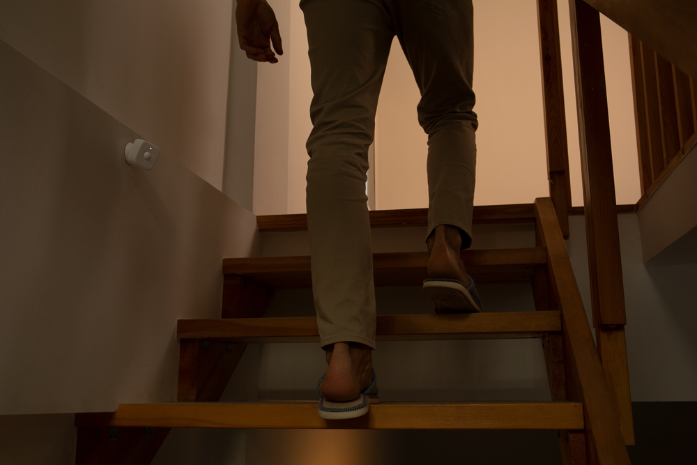 Eine Person, die eine Holztreppe hinaufsteigt. Die Person trägt Hose und Schuhe und bewegt sich nach oben in einen beleuchteten Bereich.