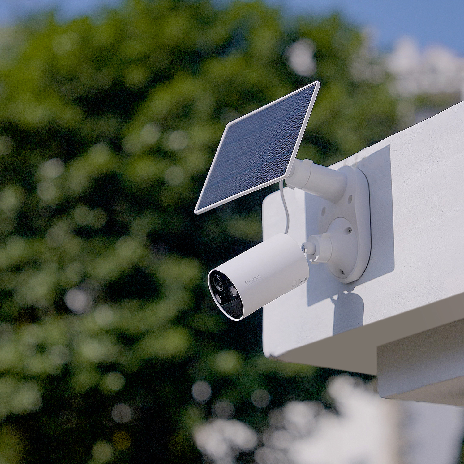 Una telecamera di sicurezza bianca con un pannello solare è montata su un muro bianco.