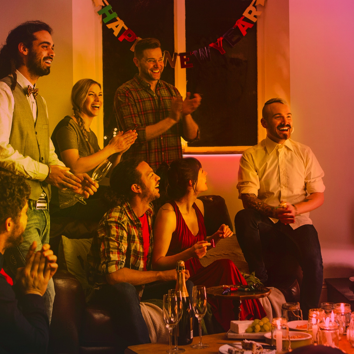 Gruppo di persone a una festa, alcuni che applaudono, altri che sorridono, con uno striscione che dice Felice Anno Nuovo.