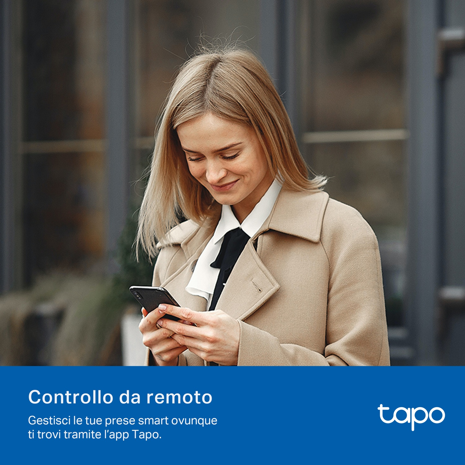 Una donna in cappotto guarda il telefono. Lo sfondo mostra un edificio e una finestra.