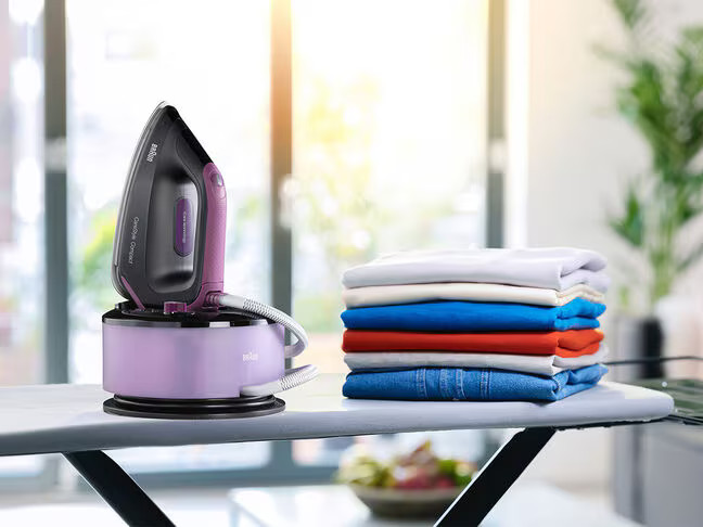 Stacja do prasowania z żelazkiem na podstawie. Obok stos złożonych ubrań.