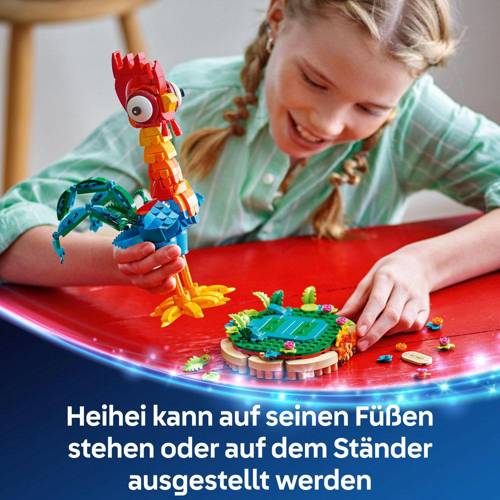 Mädchen spielt mit Lego Heihei. Roter Tischhintergrund. Buntes Lego-Huhn und Insel.