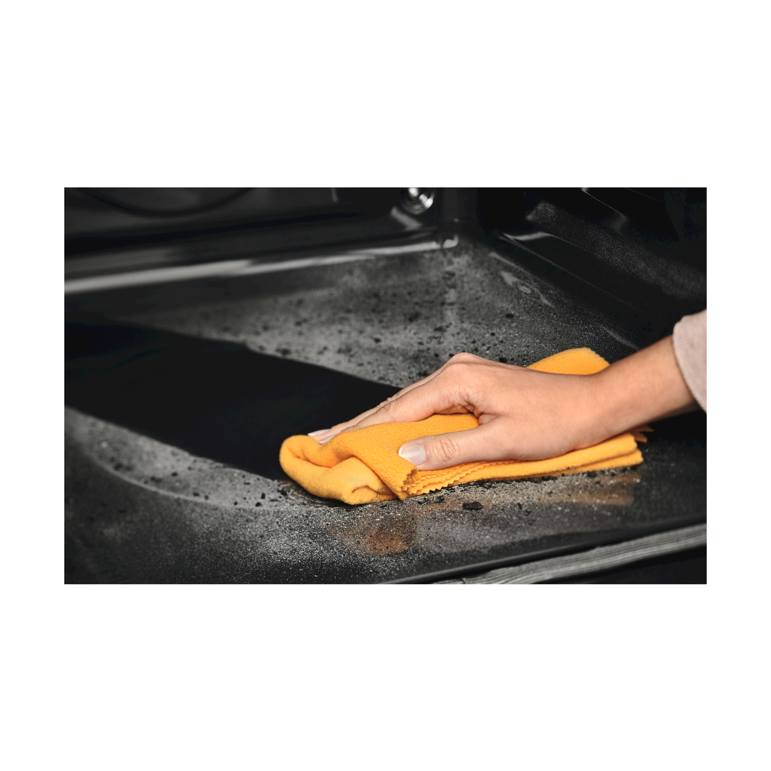 Una mano che pulisce una superficie sporca del forno con un panno arancione.